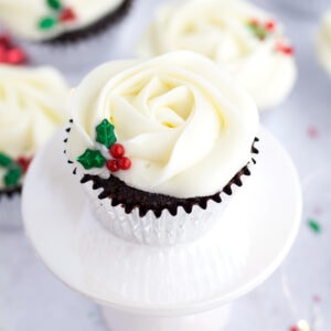 Christmas chocolate cupcake with holly berry sprinkles on white cake stand.