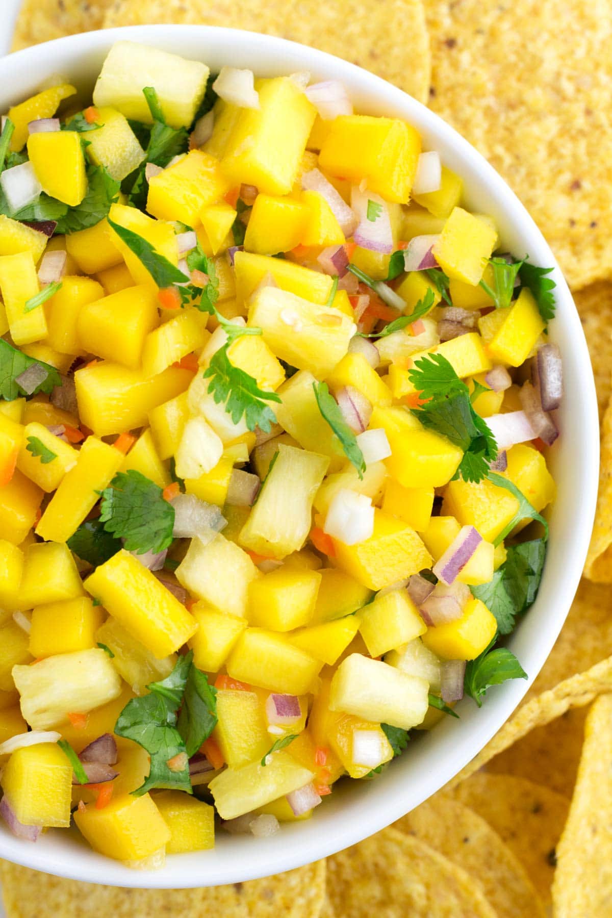 Chopped mango salsa ingredients in a bowl with chips on a platter.
