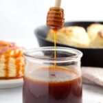 Jar of hot honey sauce with biscuits in the background.