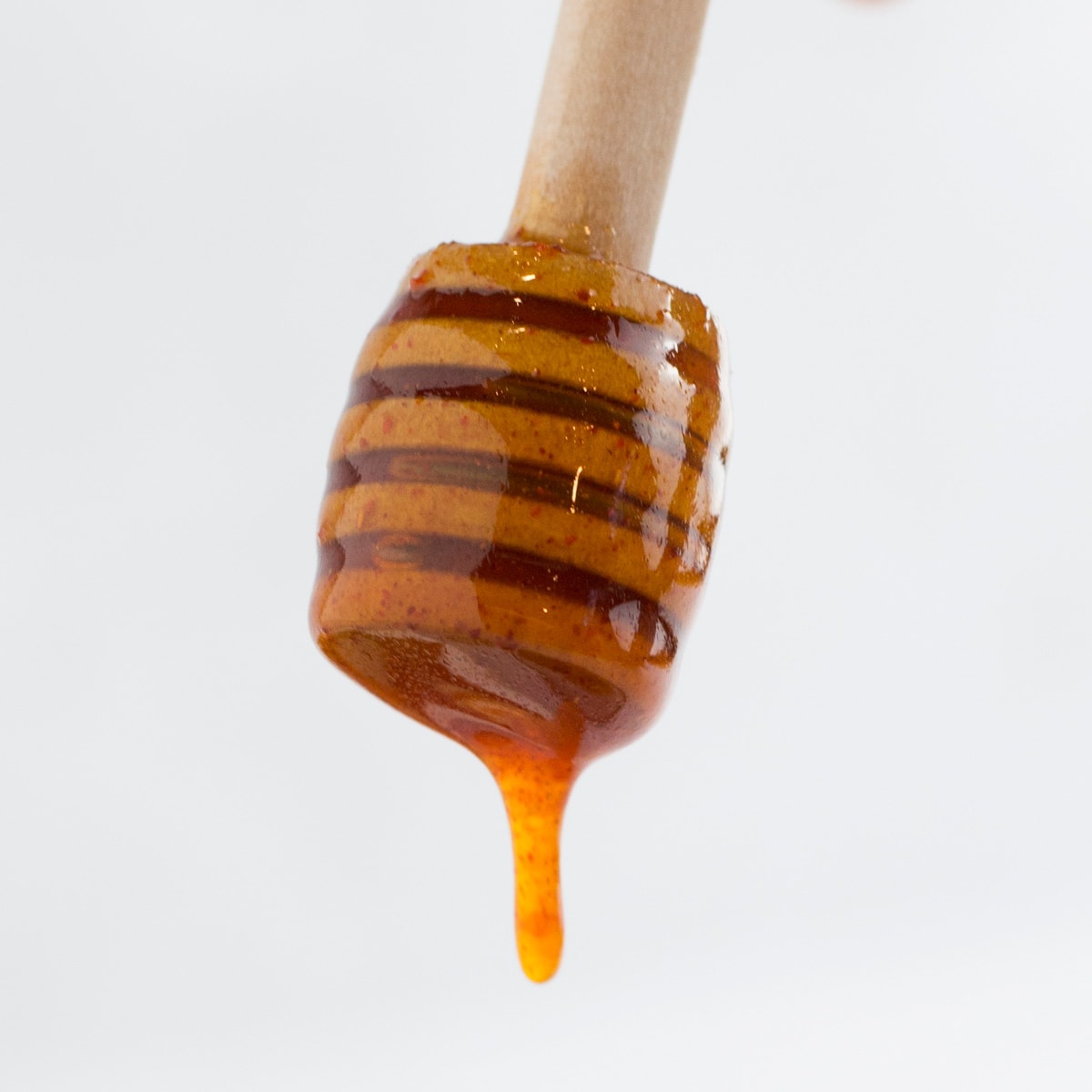 Honey dipper with spicy honey sauce falling off of it. 