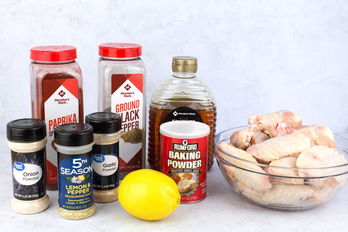 Lemon, raw chicken wings, honey, and seasonings on counter top.
