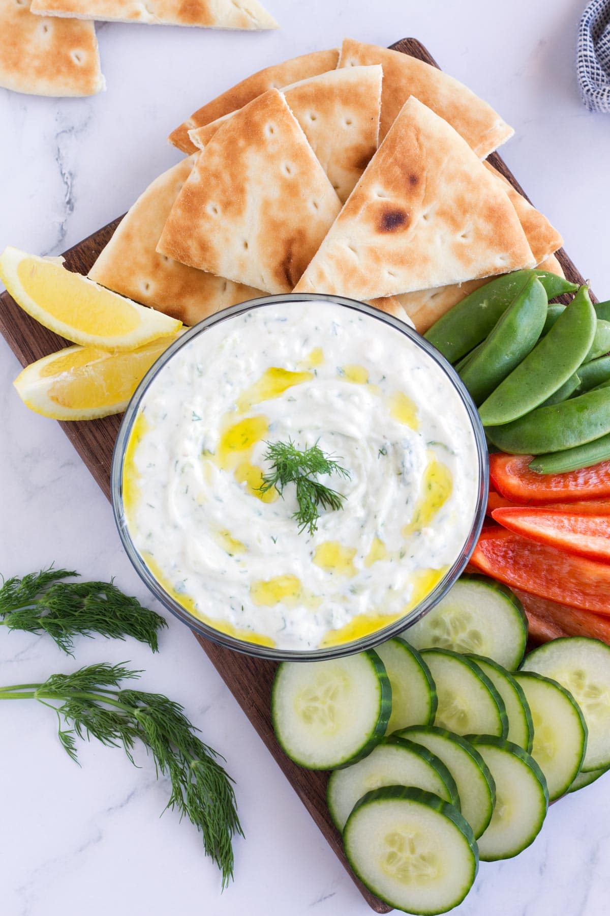 Snack board showing ways to eat tzatziki sauce with bowl of dip in the middle.