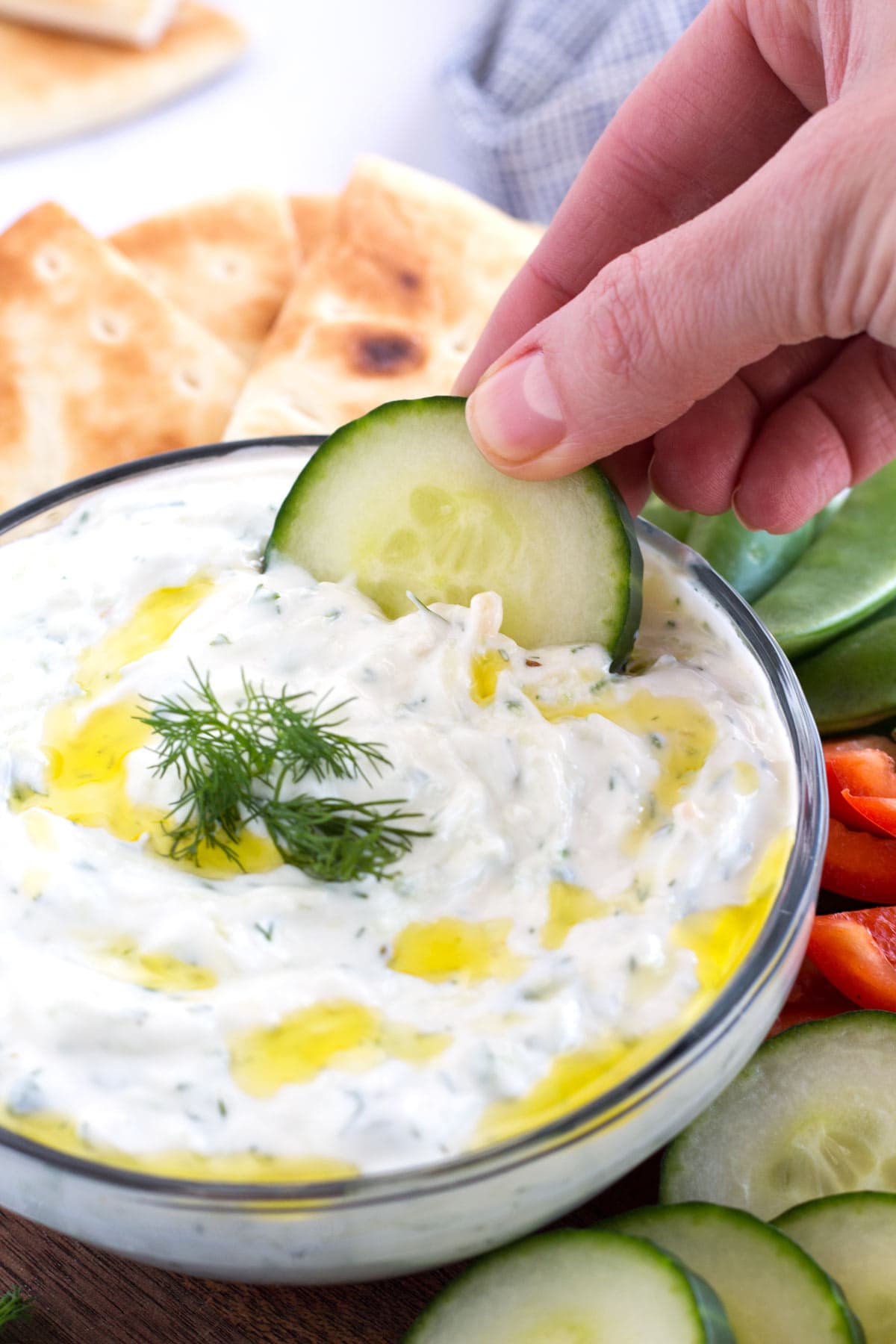 Dipping cucumber in Greek tzatziki dip with more vegetables on the side.