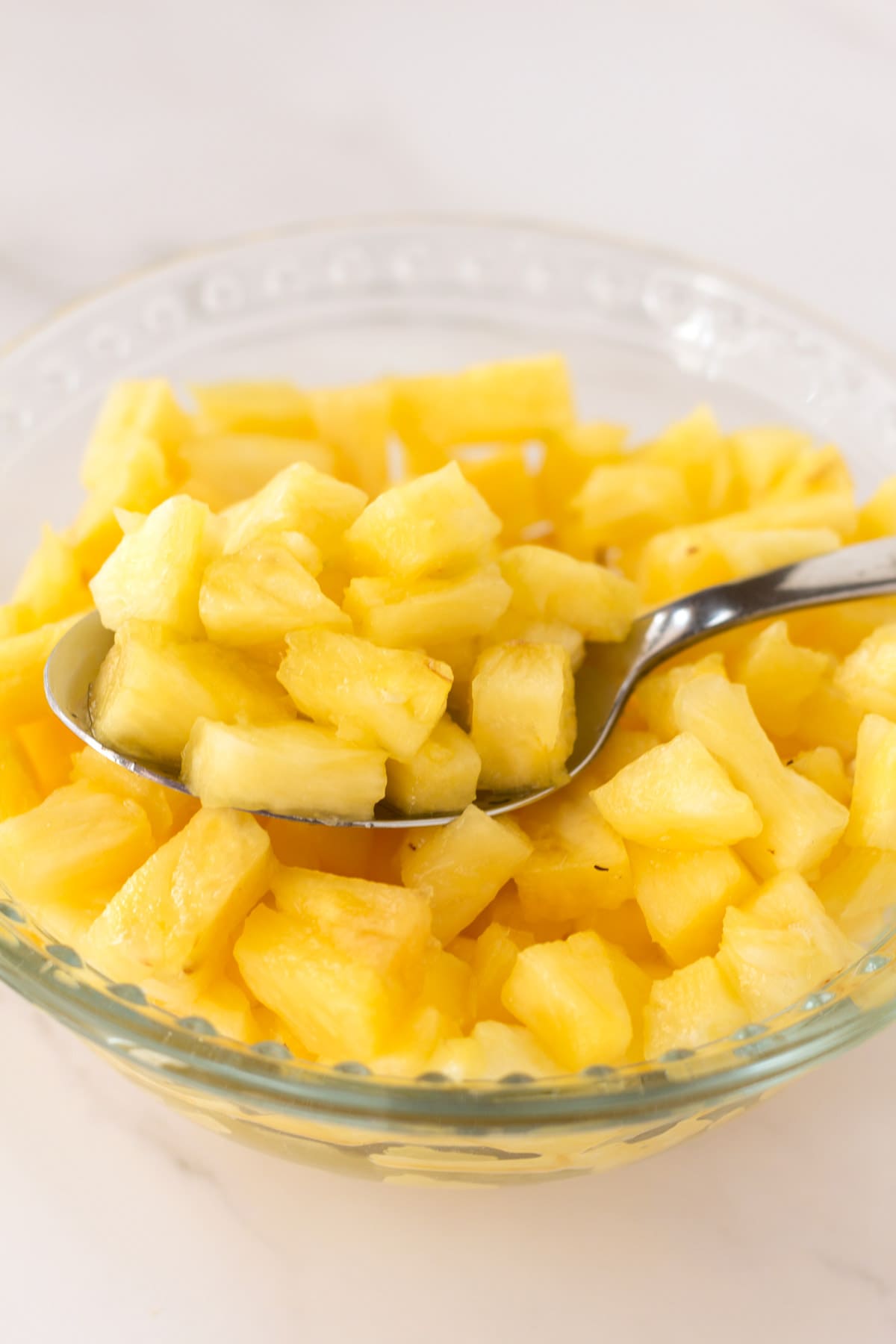 Glass bowl of chopped pineapple and a spoon.