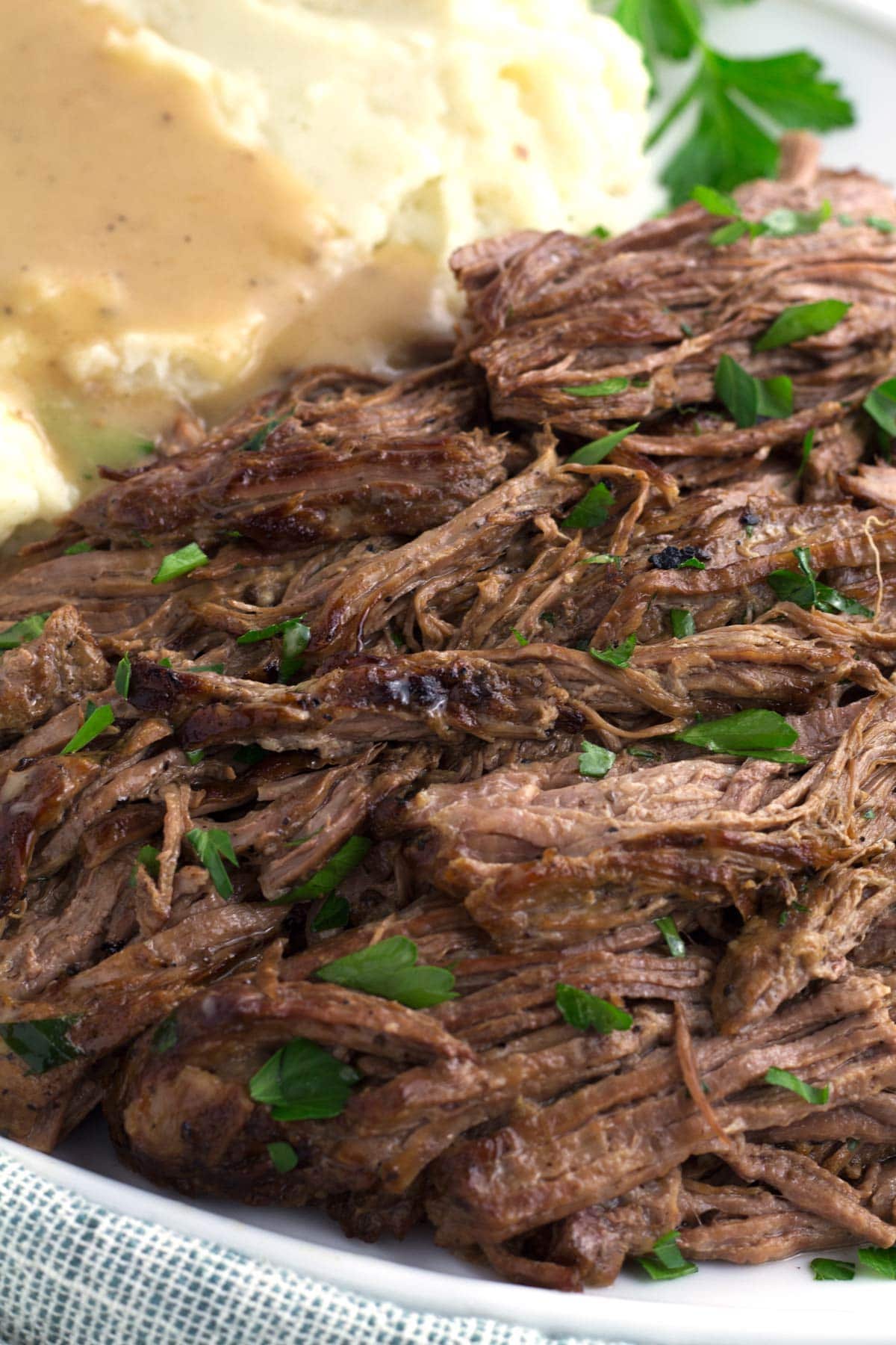 Close up of tender slow cooker tri-tip roast drizzled with gravy and fresh parsley.