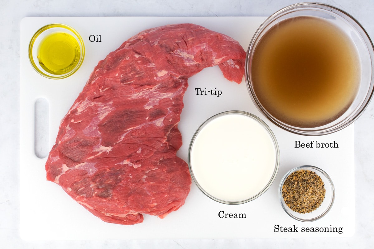 Beef roast, cream, seasoning, oil, and broth on a white cutting board.