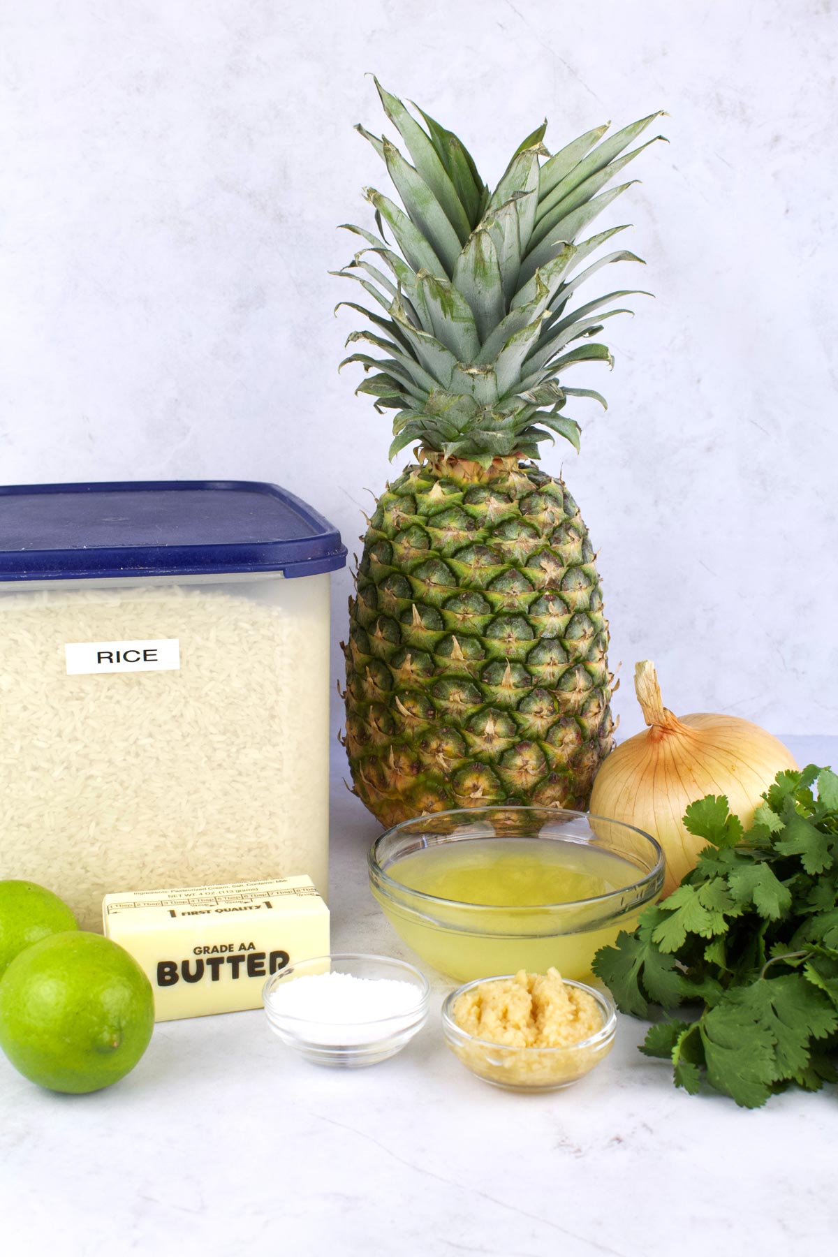 Pineapple, rice, limes, cilantro, and other ingredients on white counter top.