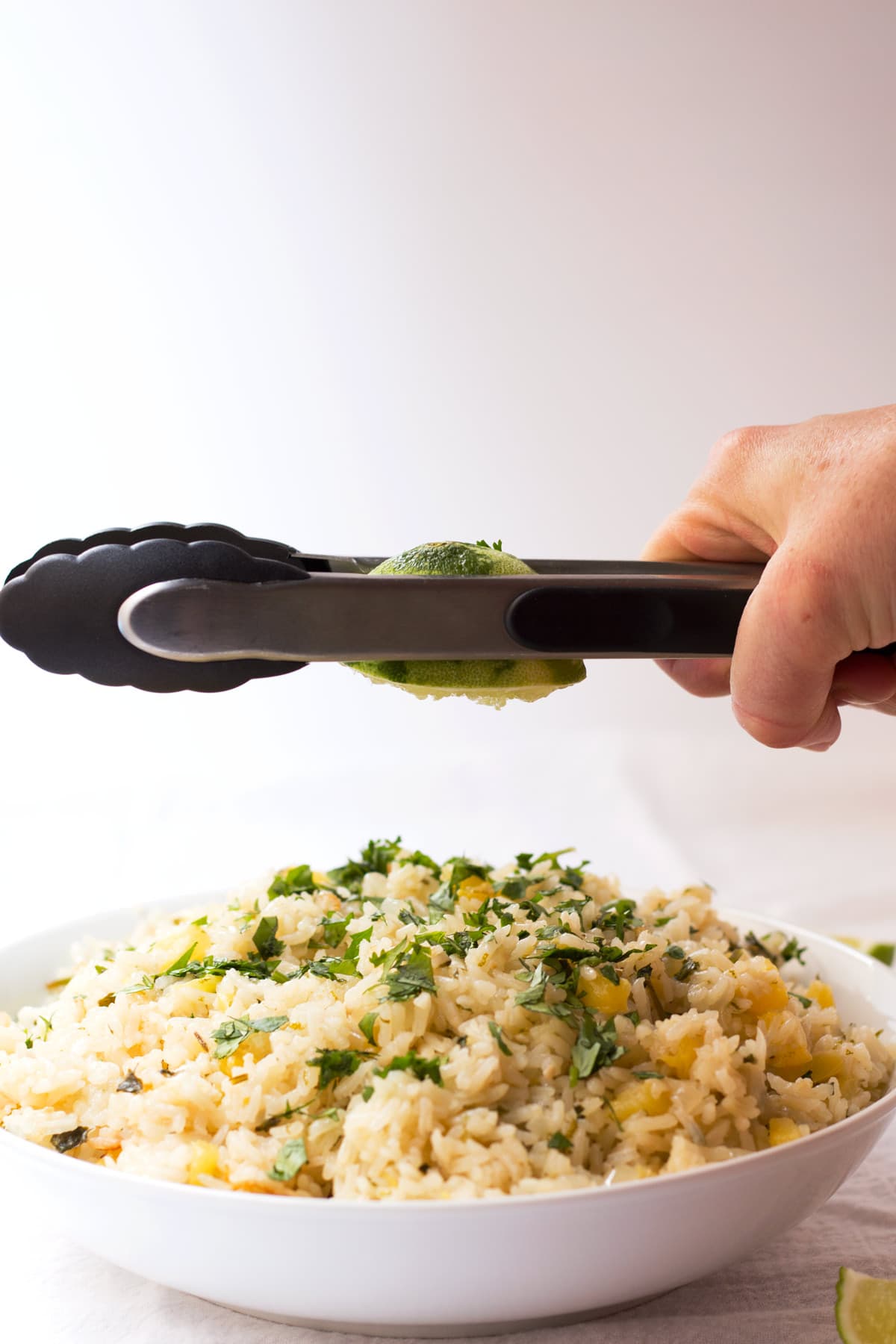 Hand squeezing a lime with tongs over a bowl of pineapple lime rice.
