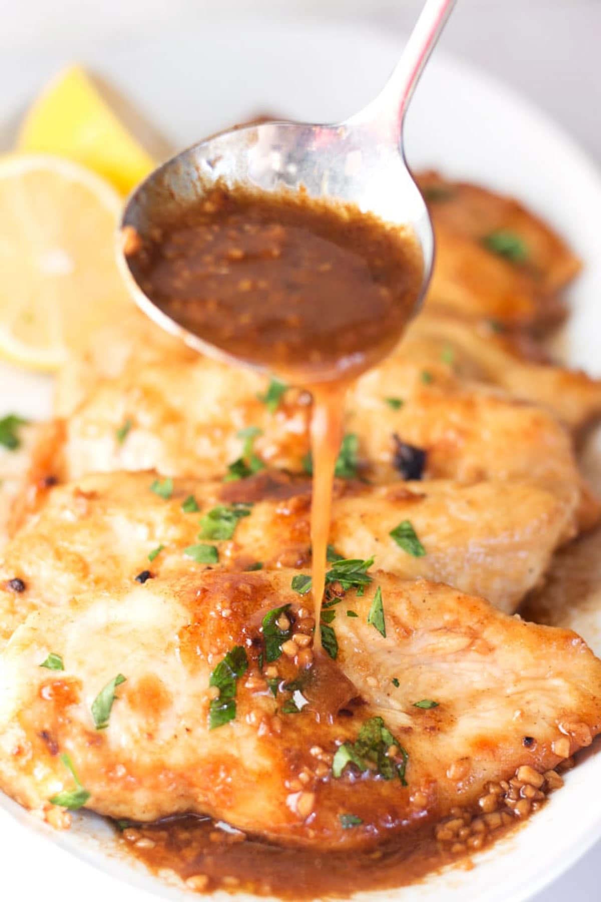 Ladle pouring garlic lemon sauce on a row of chicken breasts.