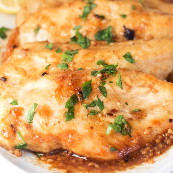 Three golden brown chicken breasts with lemon sauce and parsley on a plate.