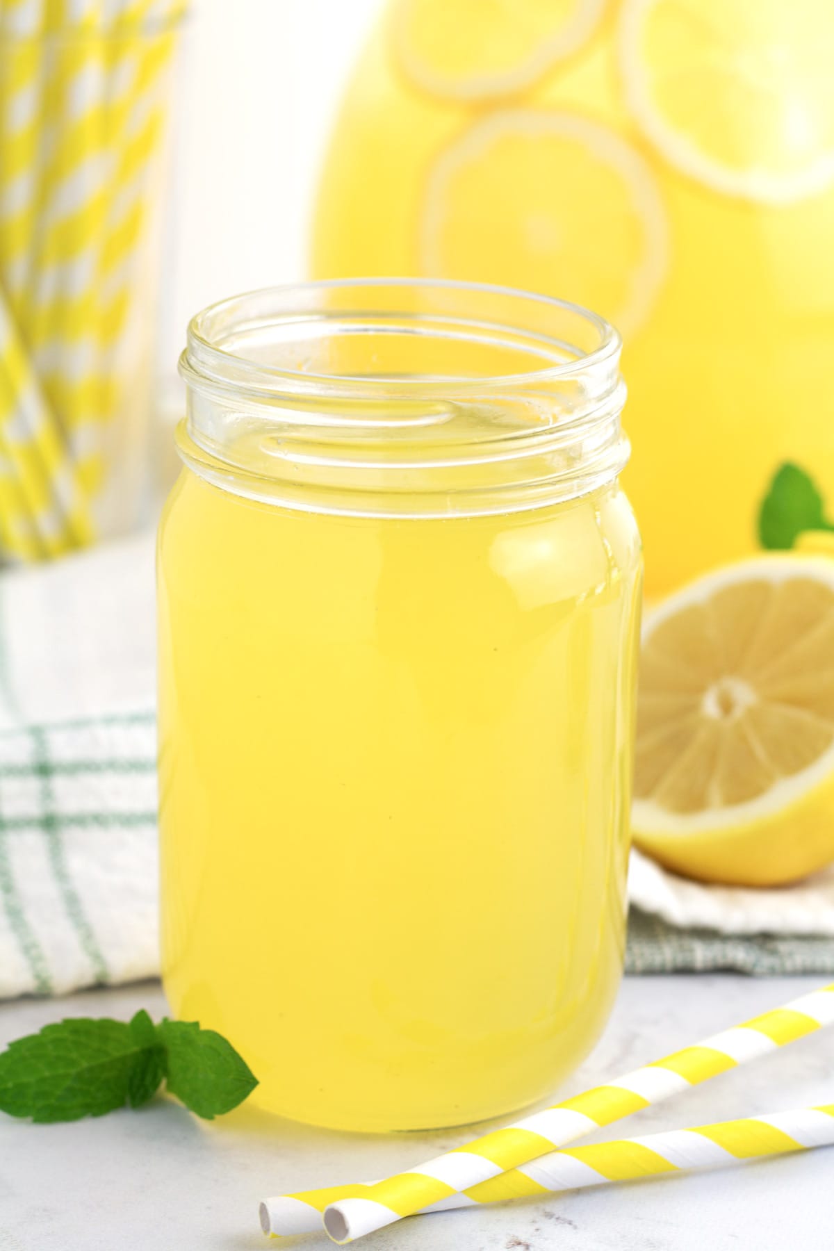 Clear glass jar of yellow lemonade concentrate with yellow straws laying beside it.