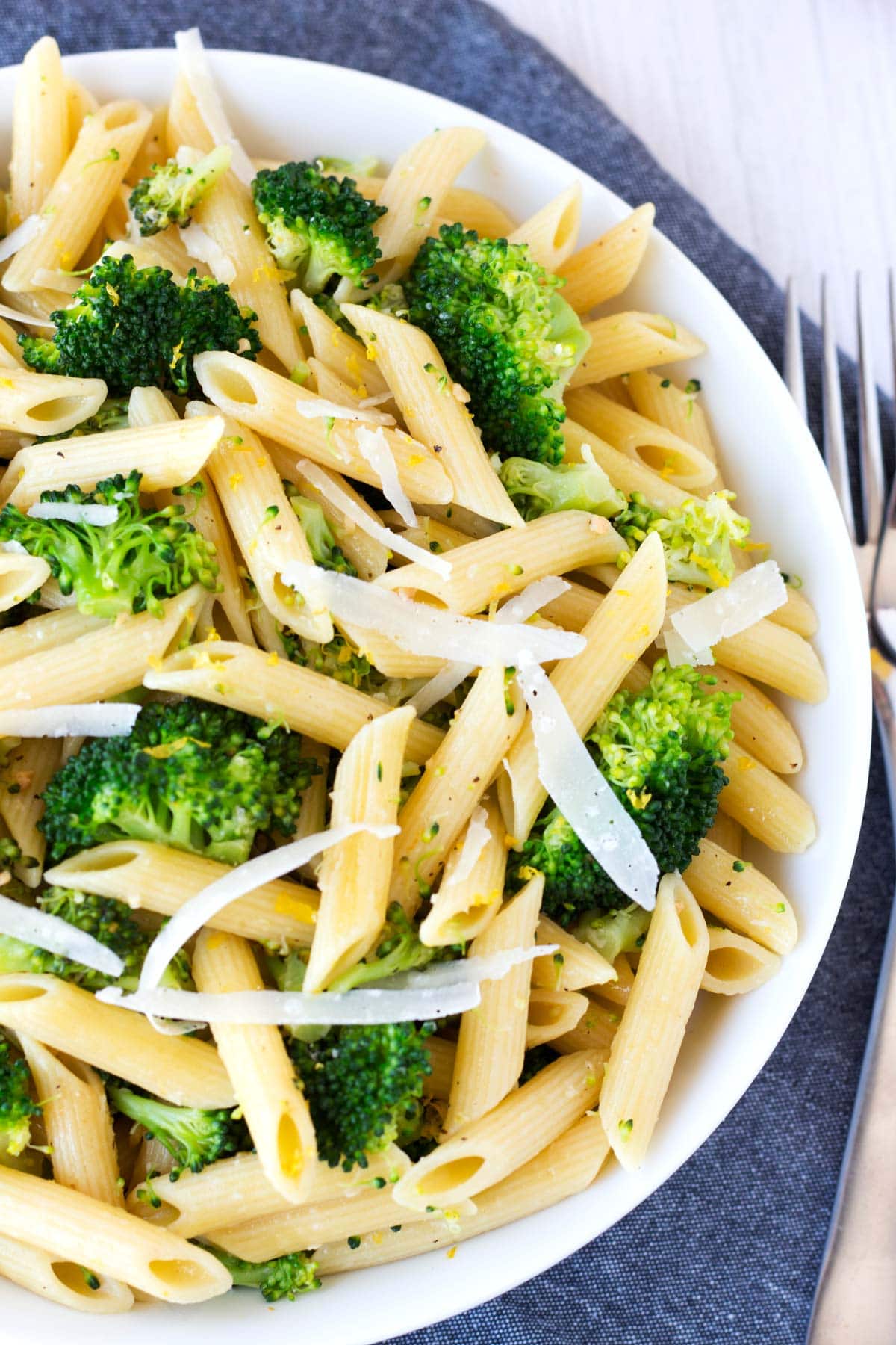 Overhead bowl of pasta with broccoli with forks on the side and a gray towel underneath.