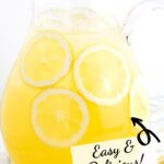 Glass pitcher of lemonade with lemonade slices inside and text overlay on top.
