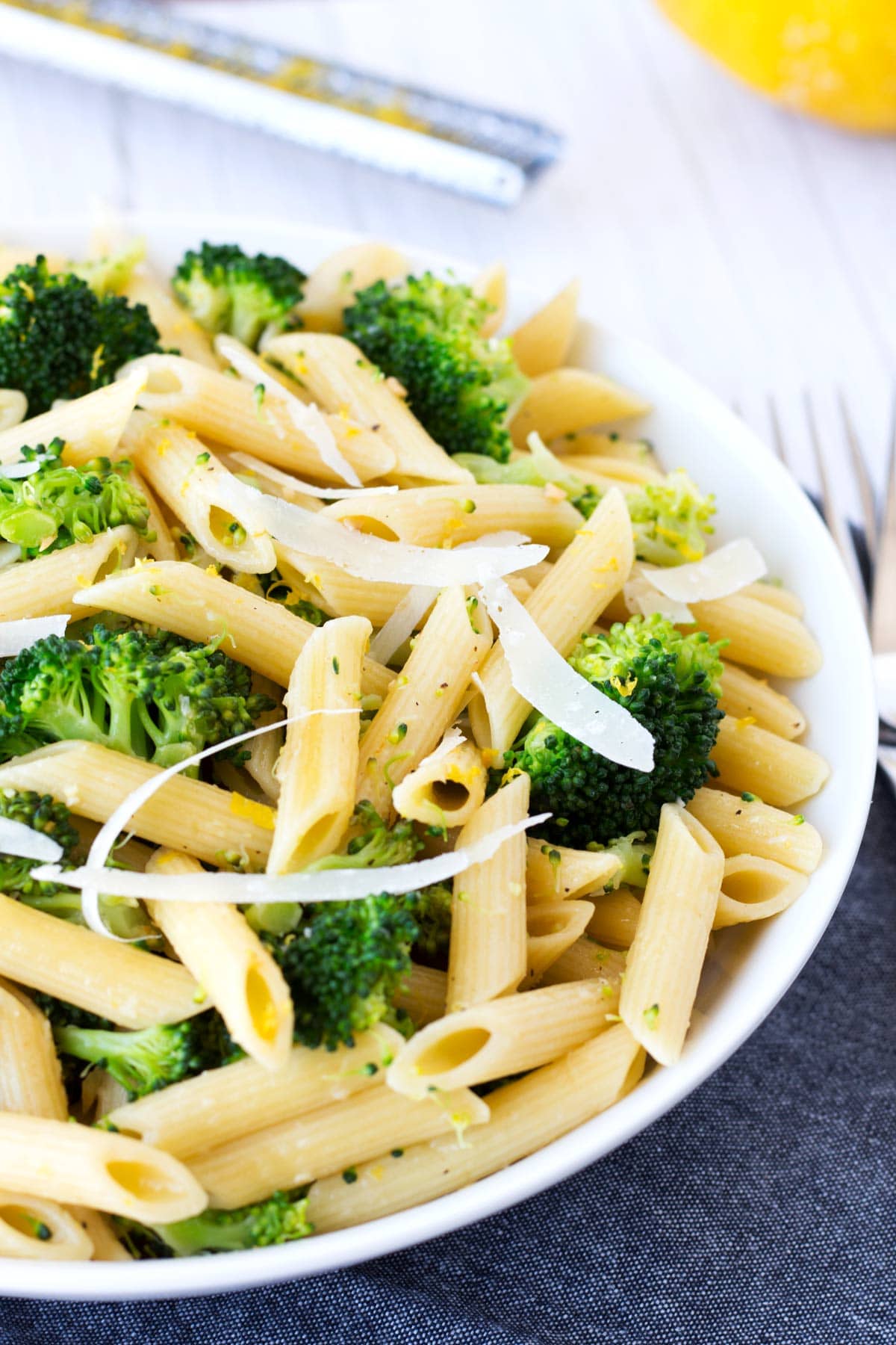 Pasta with broccoli, grated parmesan, and lemon sauce in a white bowl with a gray towel and forks on the side.