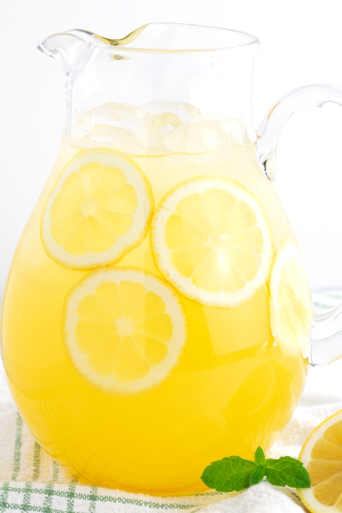 Glass pitcher of lemonade with lemonade slices inside and fresh mint laying on the side.