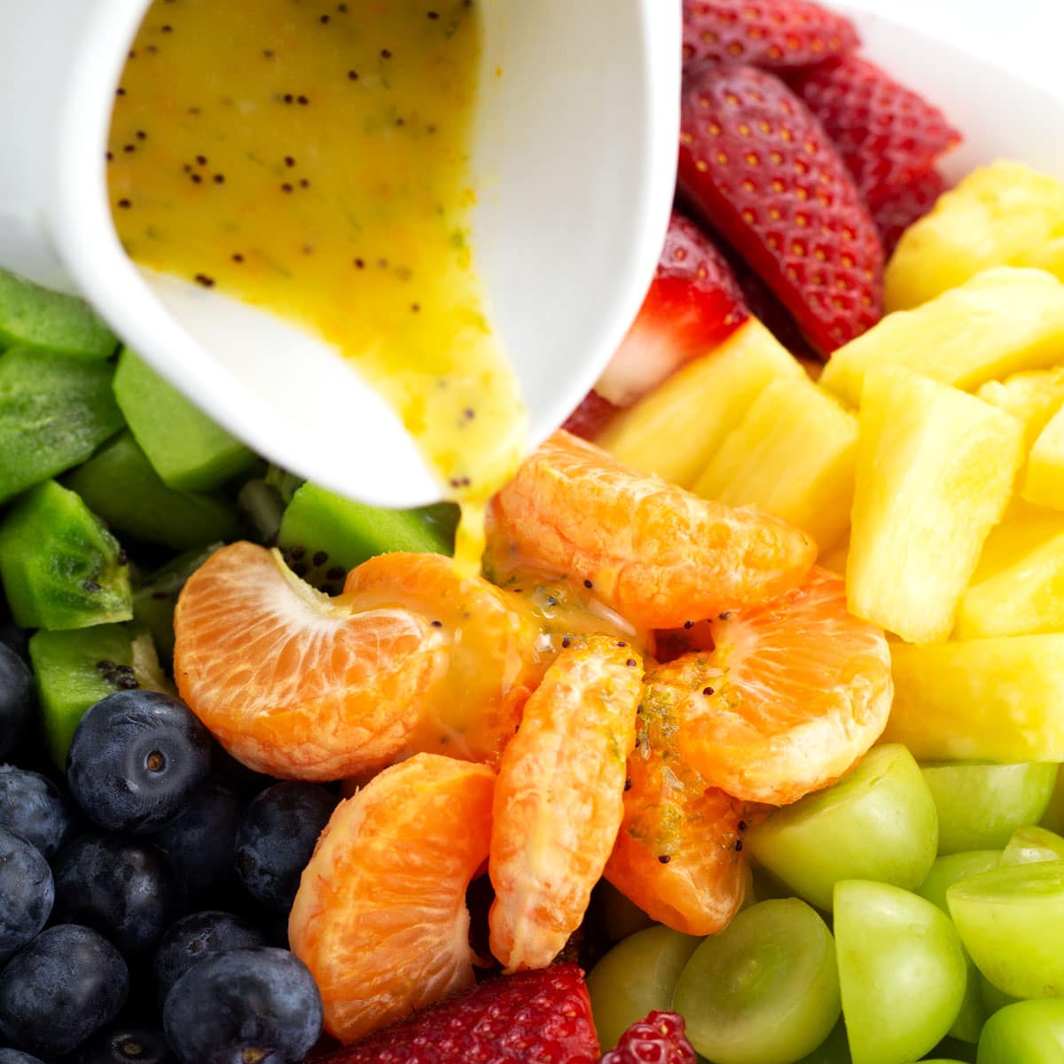 Pouring fruit salad dressing over bowl of fresh fruit.