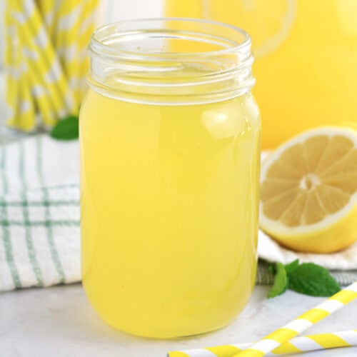 Clear glass jar of yellow lemonade concentrate with yellow straws in background.