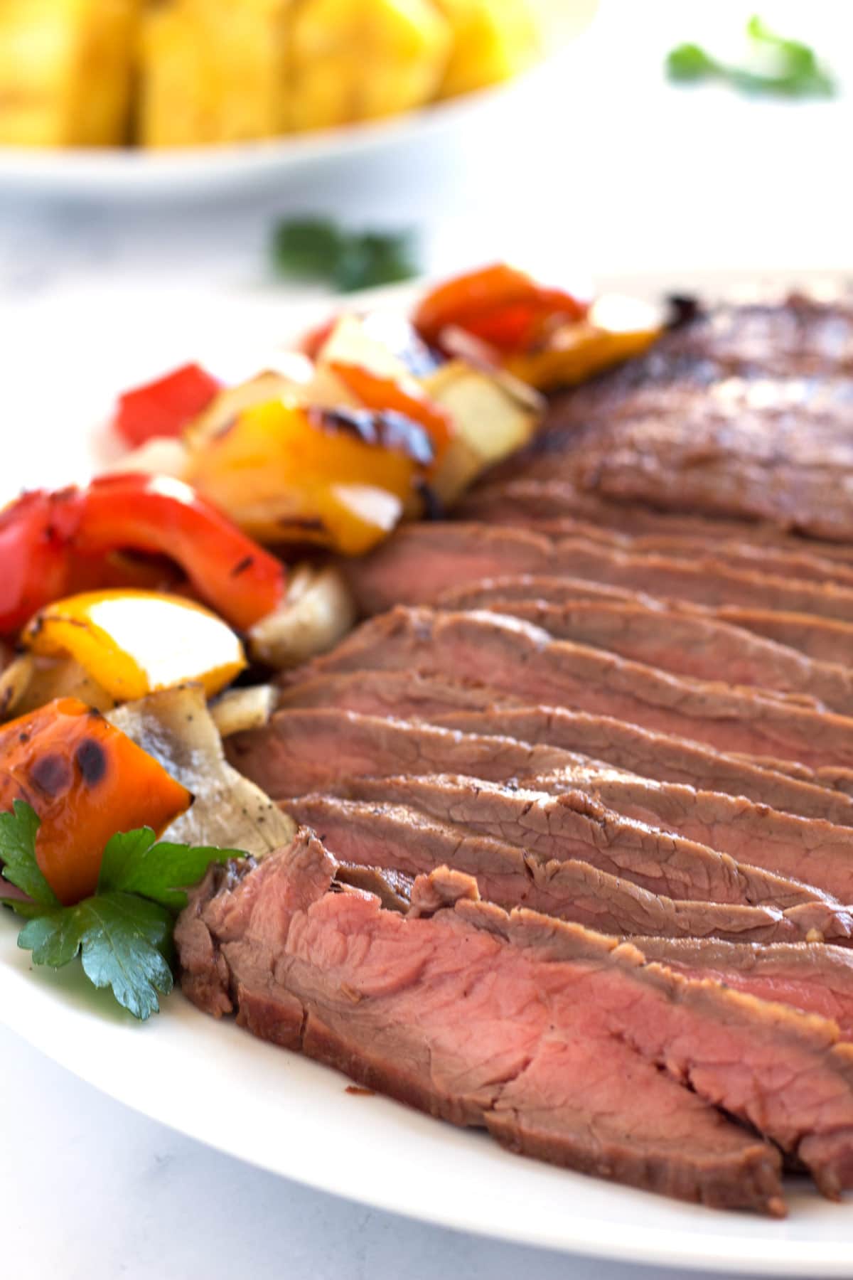 Flank steak with soy sauce marinade sliced on white platter with grilled veggies.