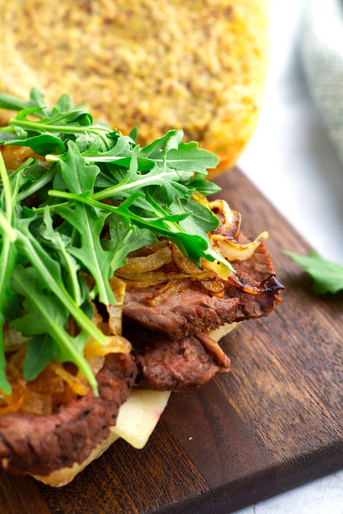 Open faced leftover tri tip sandwich with arugula on top, onions underneath, and extra bread in the background.