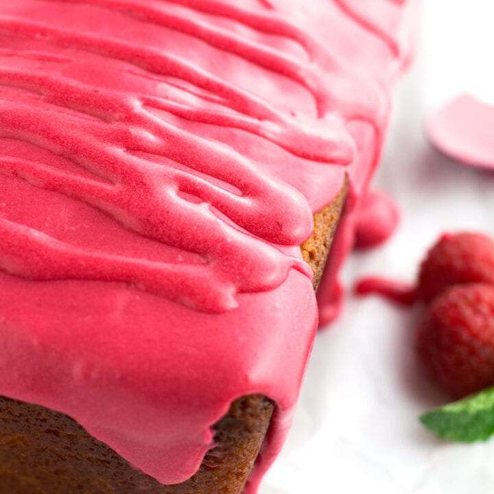 The perfect texture of raspberry glaze on the edge of cake with fresh raspberries and mint in the background.
