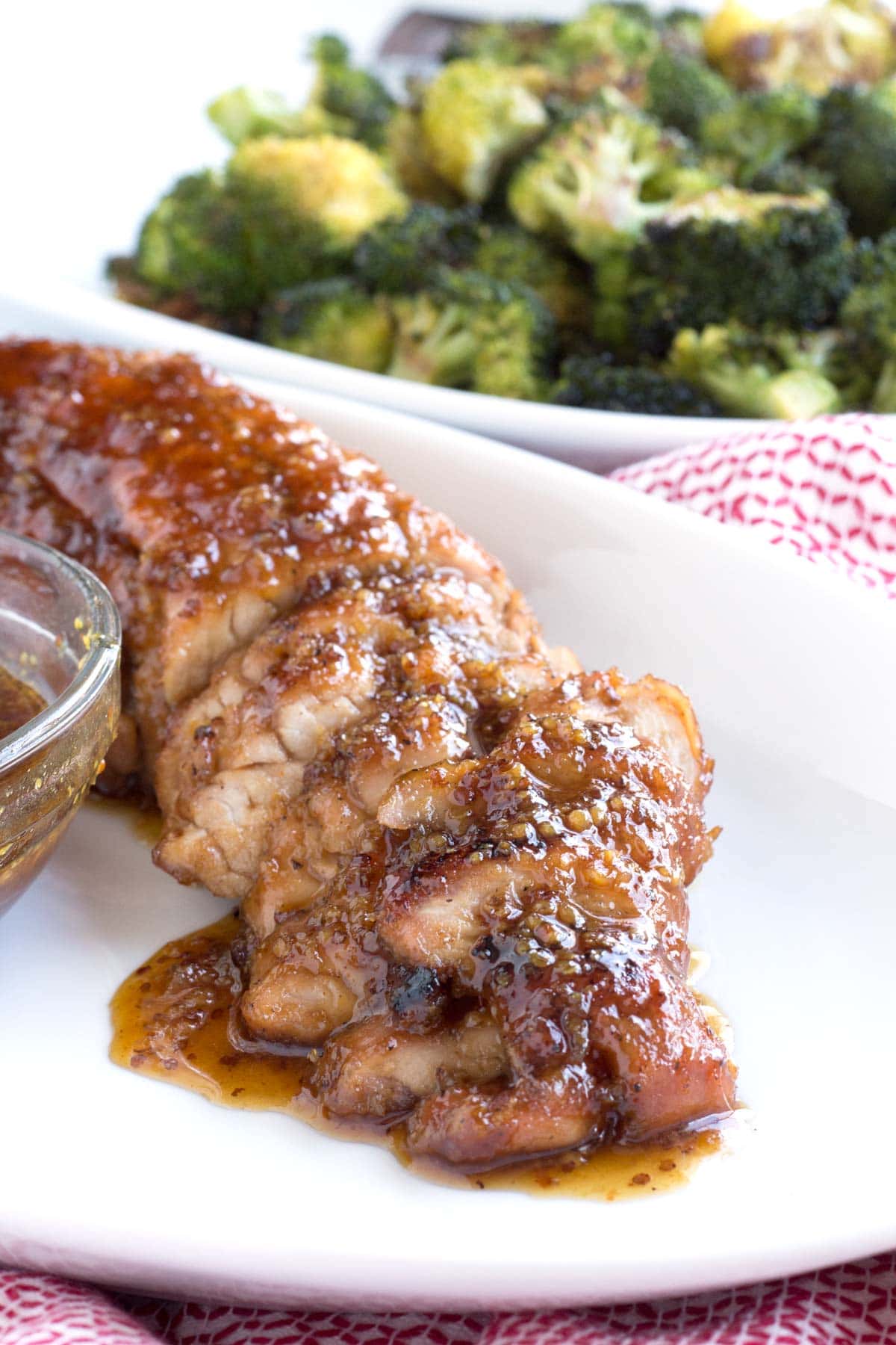 Slices of the best pork tenderloin on a serving plate with broccoli in the background.