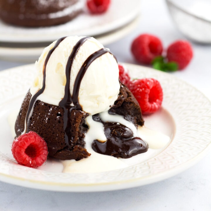 Individual molten chocolate lava cake with oozy center with scoop of ice cream and raspberries on a plate.