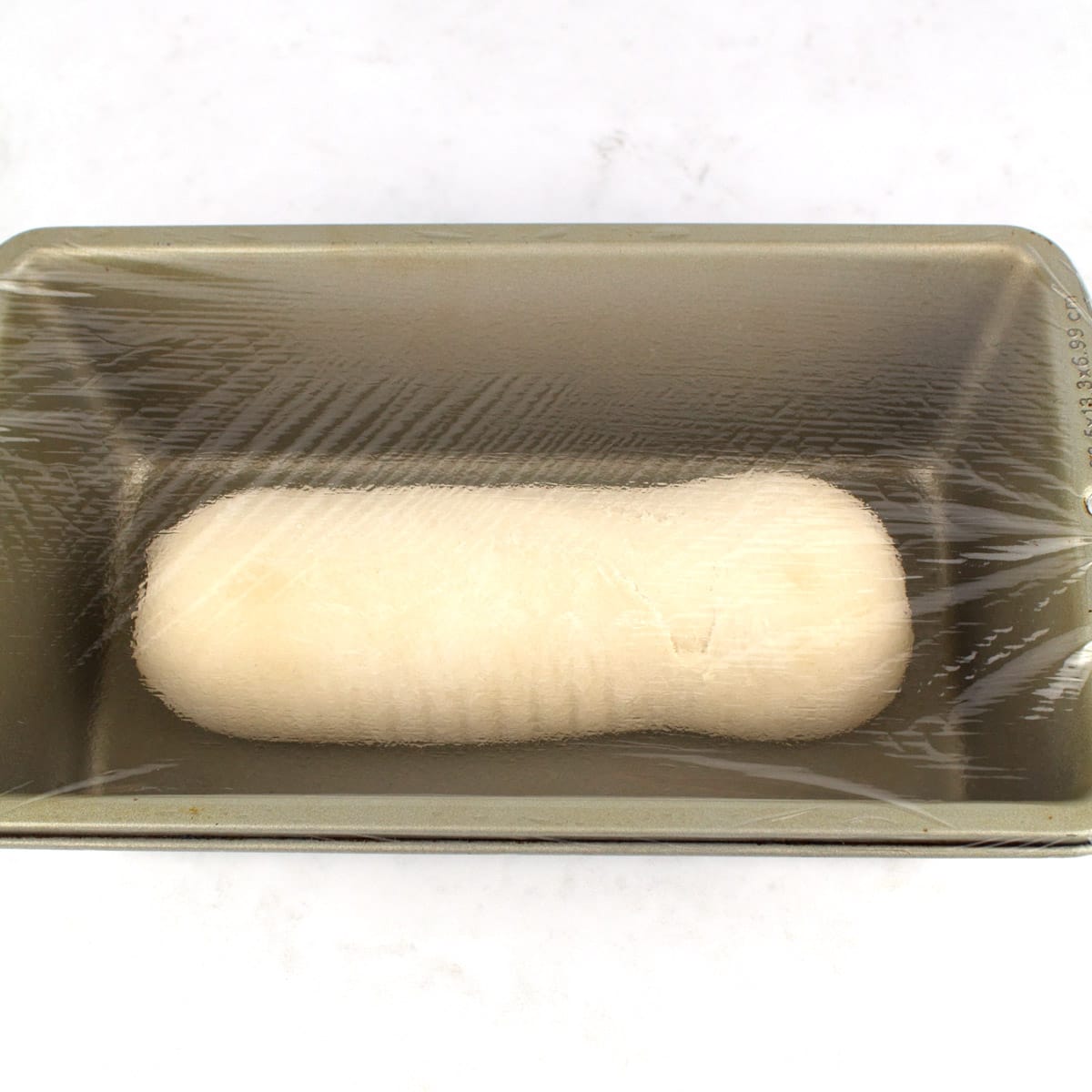 Rhodes bread dough frozen in a loaf pan with plastic wrap over the top.