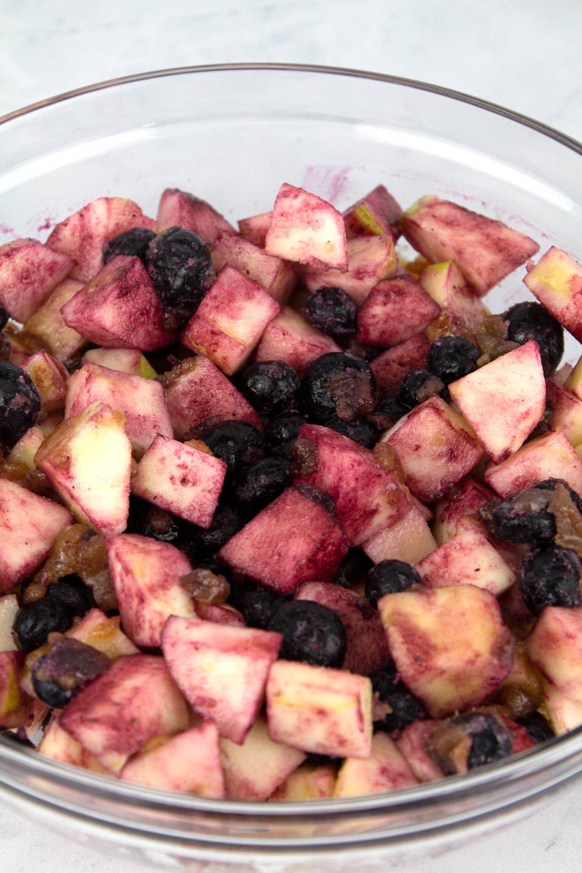 Glass bowl of apple chunks and frozen blueberries covered in sugar and flour.