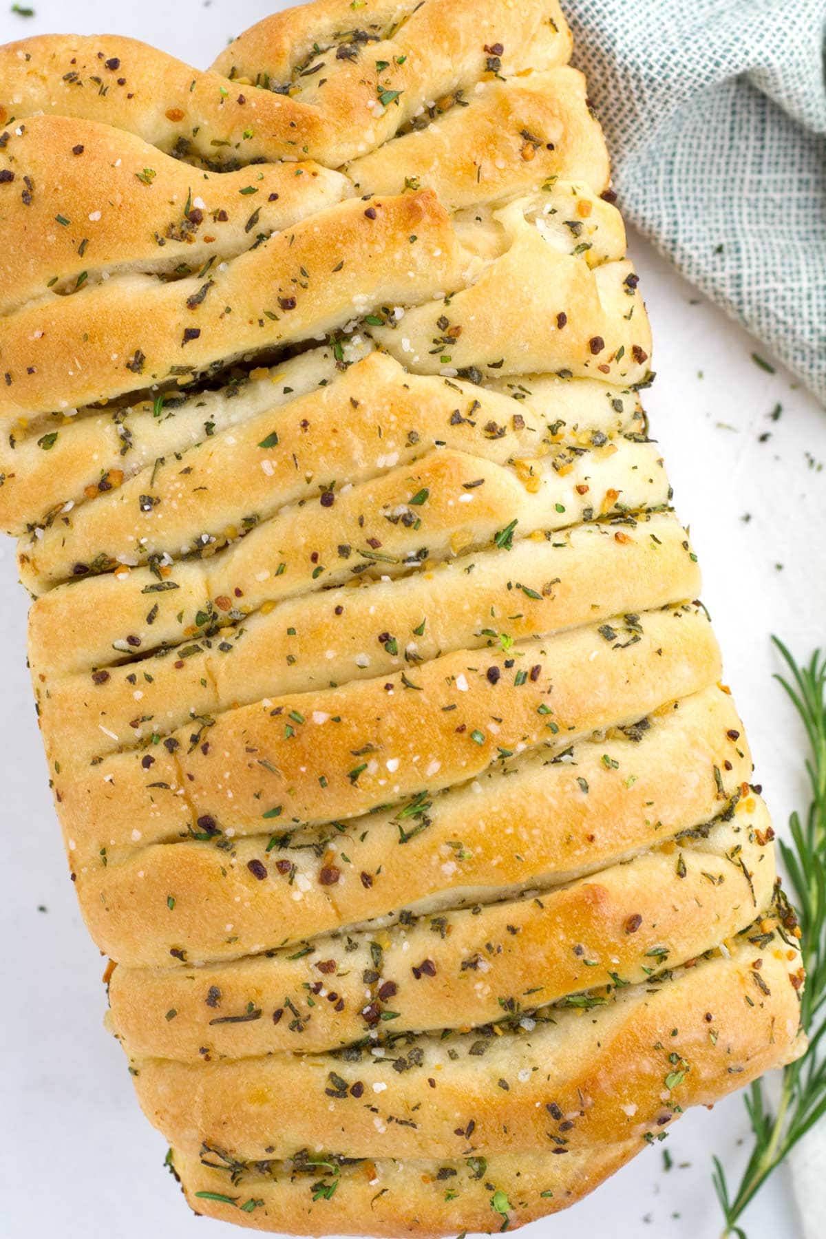 Golden brown loaf of savory pull apart bread with fresh rosemary on the side.