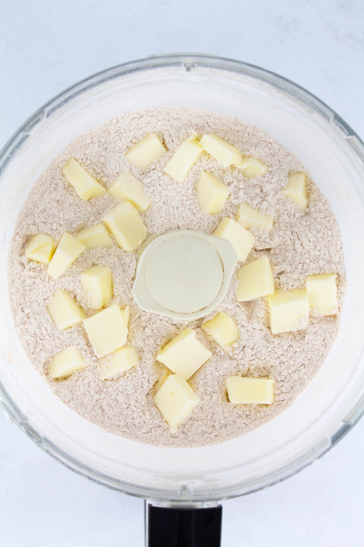 Overhead of food processor with dry ingredients and chunks of butter.