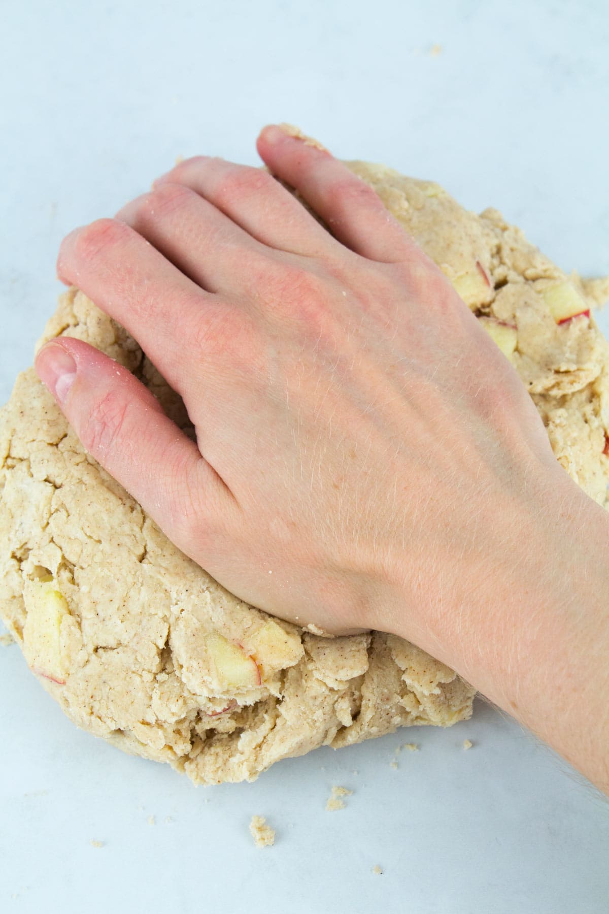 Hand kneading the apple scone dough on a white counter.