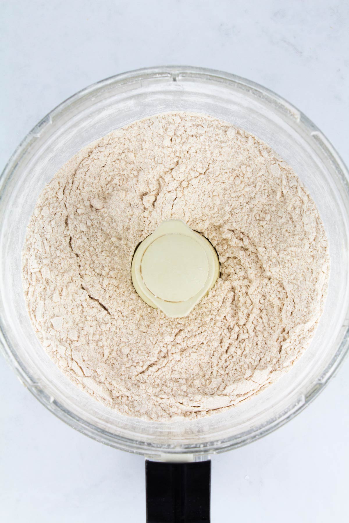 Overhead of food processor with moist dry ingredients after adding butter.