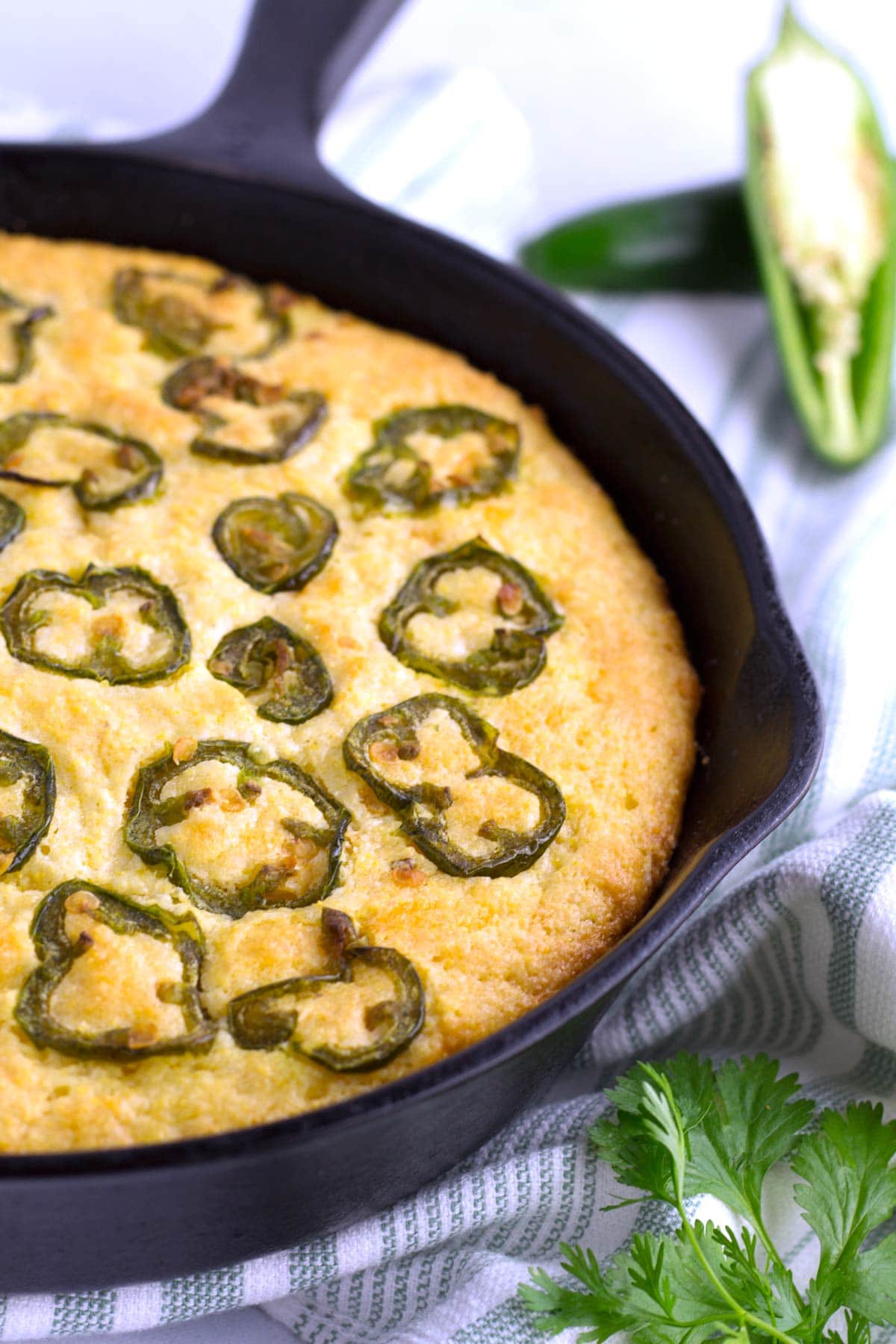 Skillet of jalapeno cornbread with towel and cilantro.