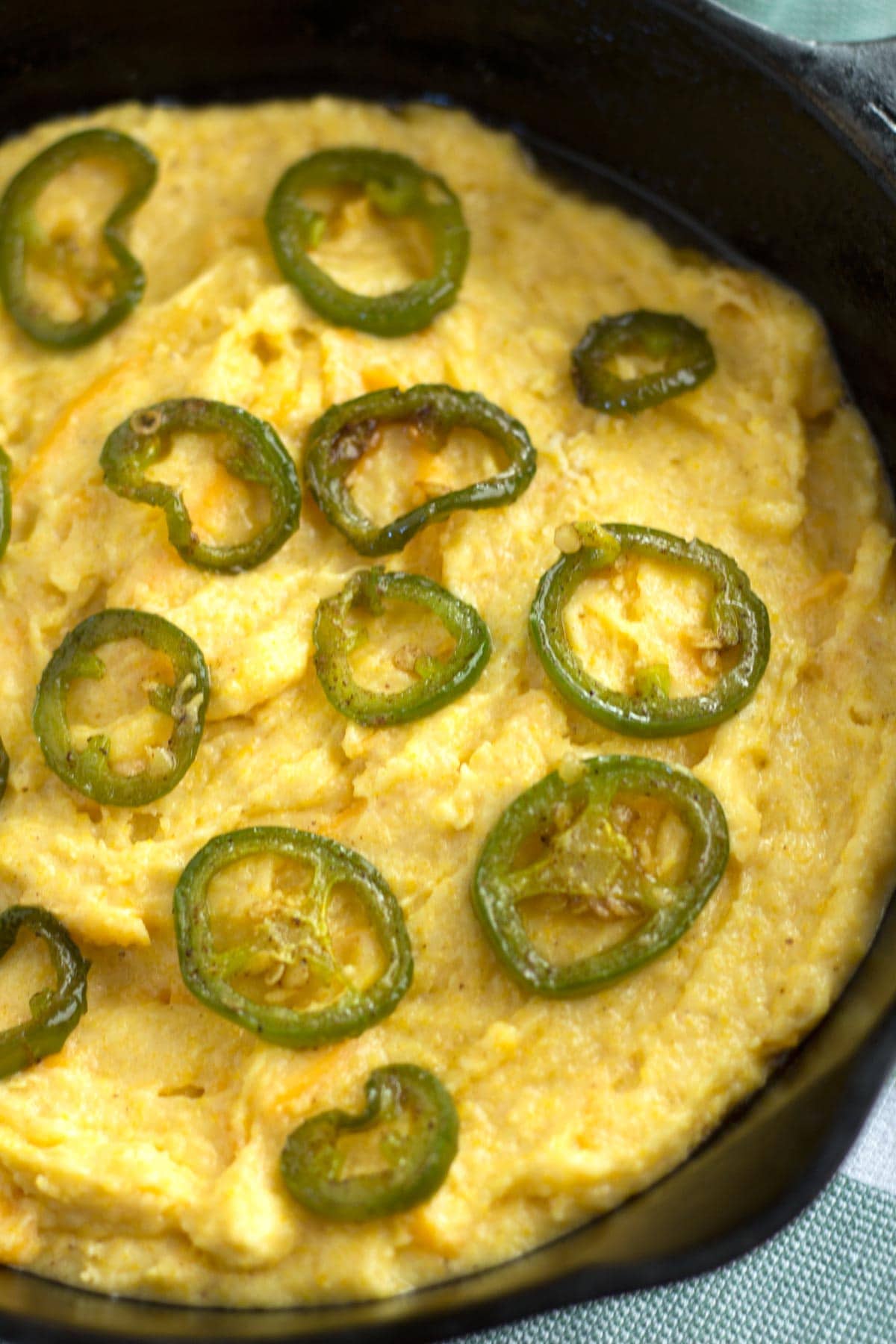 Raw cornbread with slices of jalapenos placed around the skillet.
