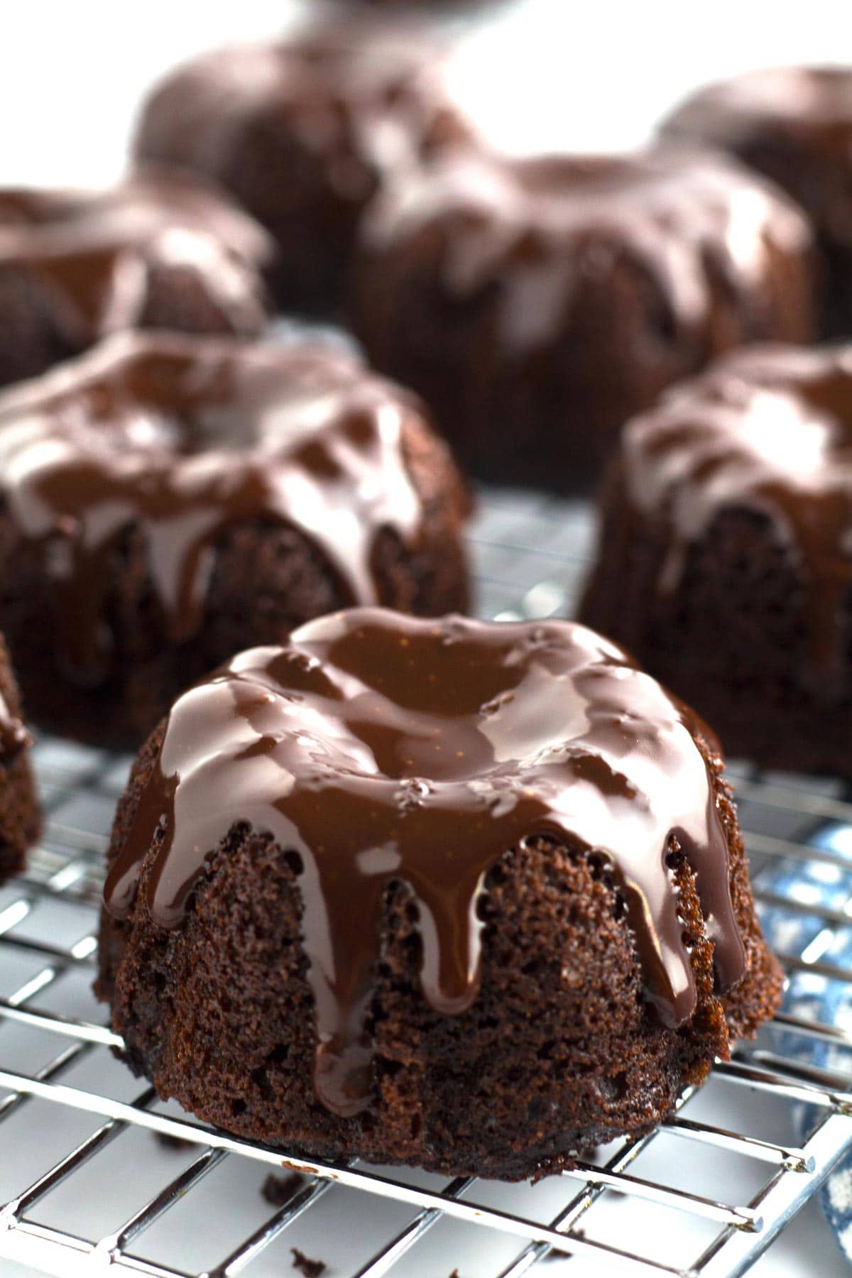 Mini Bundt Cakes decorated with chocolate ganache on cooling rack.