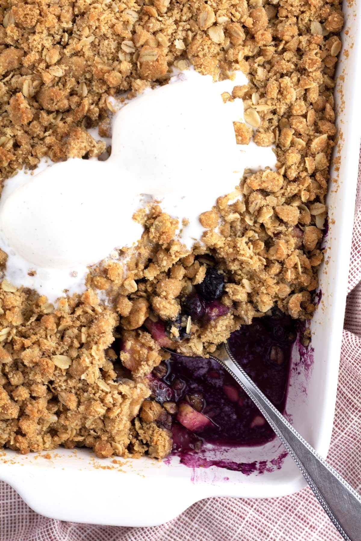 Overhead of blueberry apple crisp with vanilla ice cream and a serving spoon.