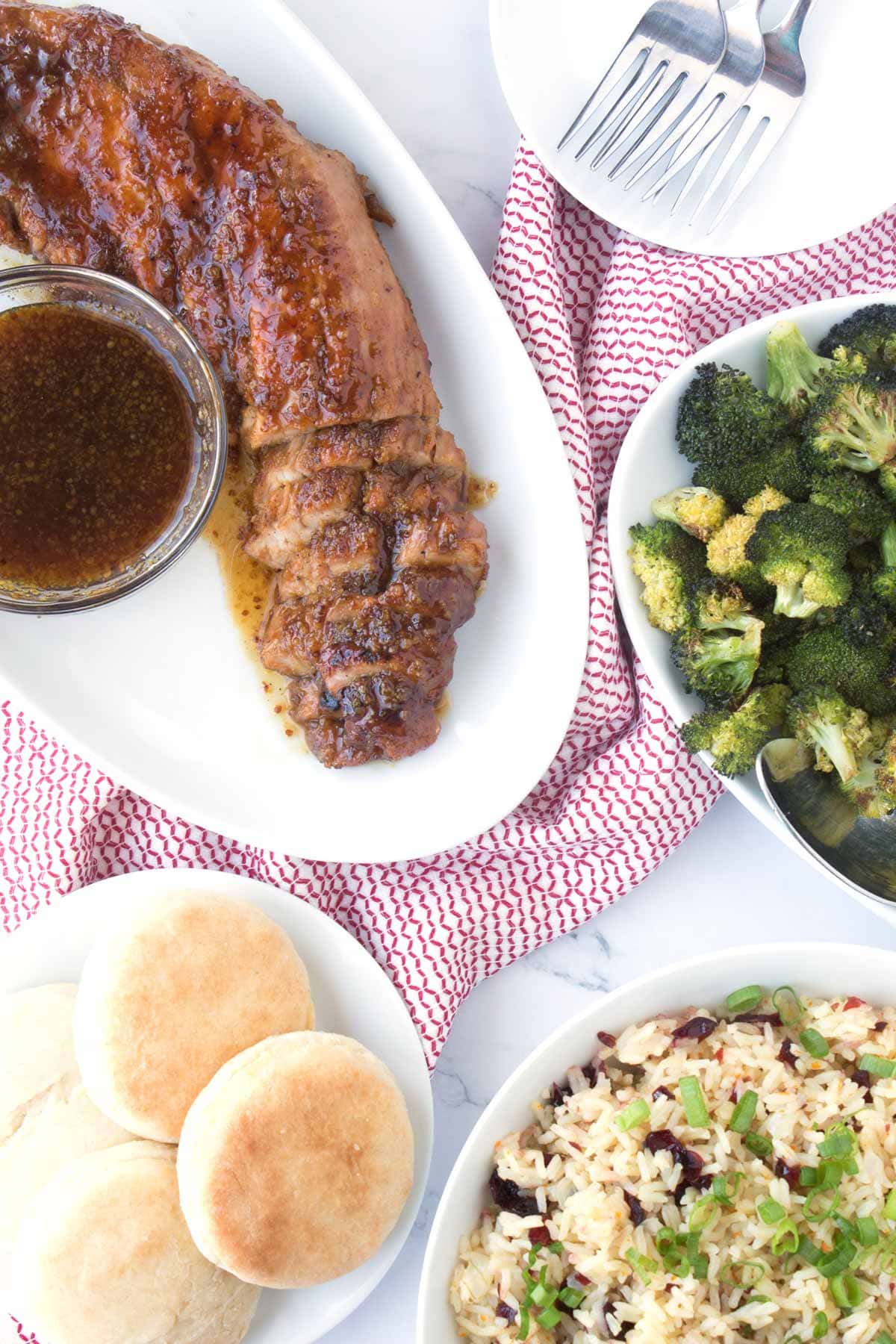 Table with pork tenderloin, biscuits, broccoli and rice.
