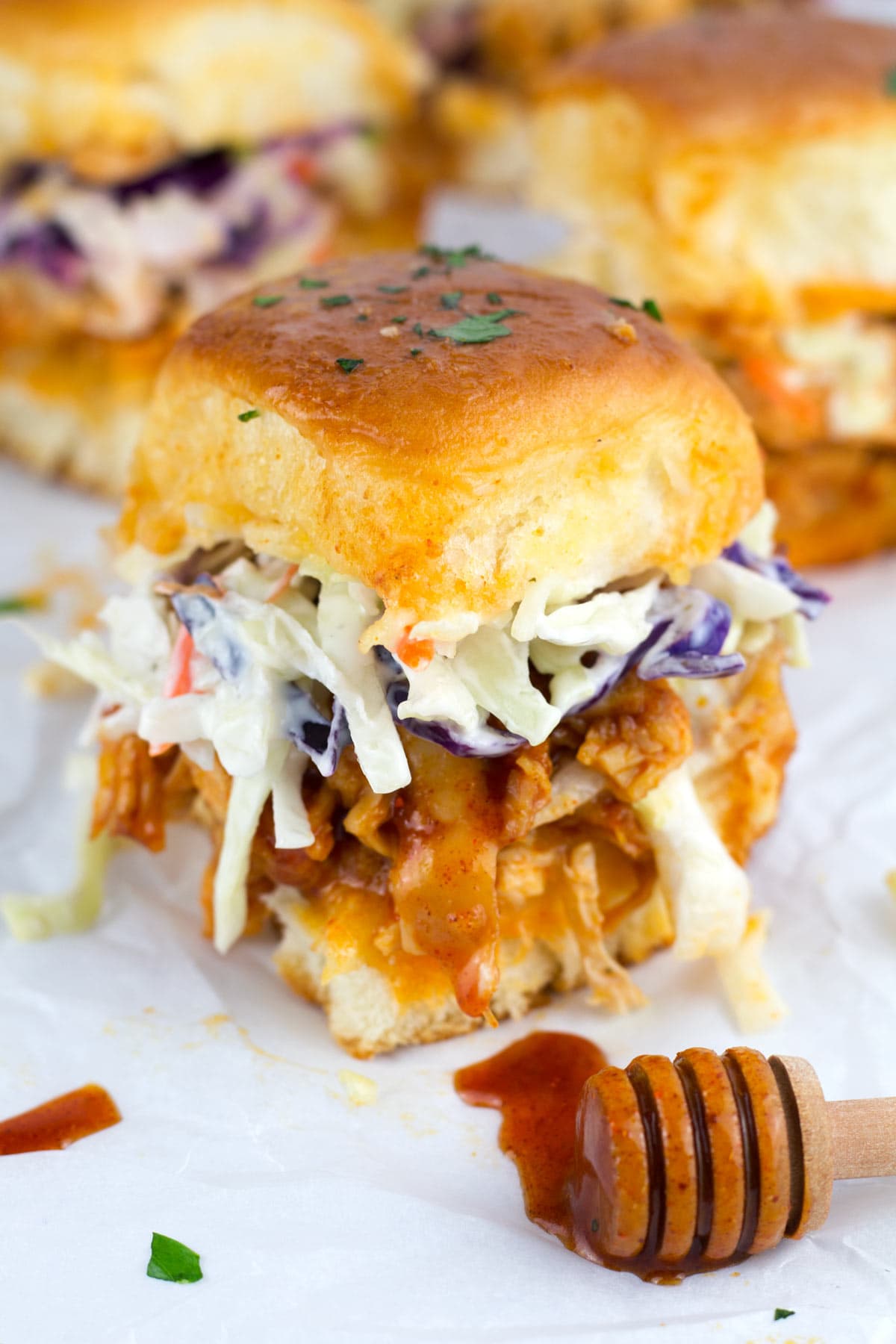 Super up close view of layers of Hawaiian rolls, cheese, shredded chicken, and coleslaw on sliders.