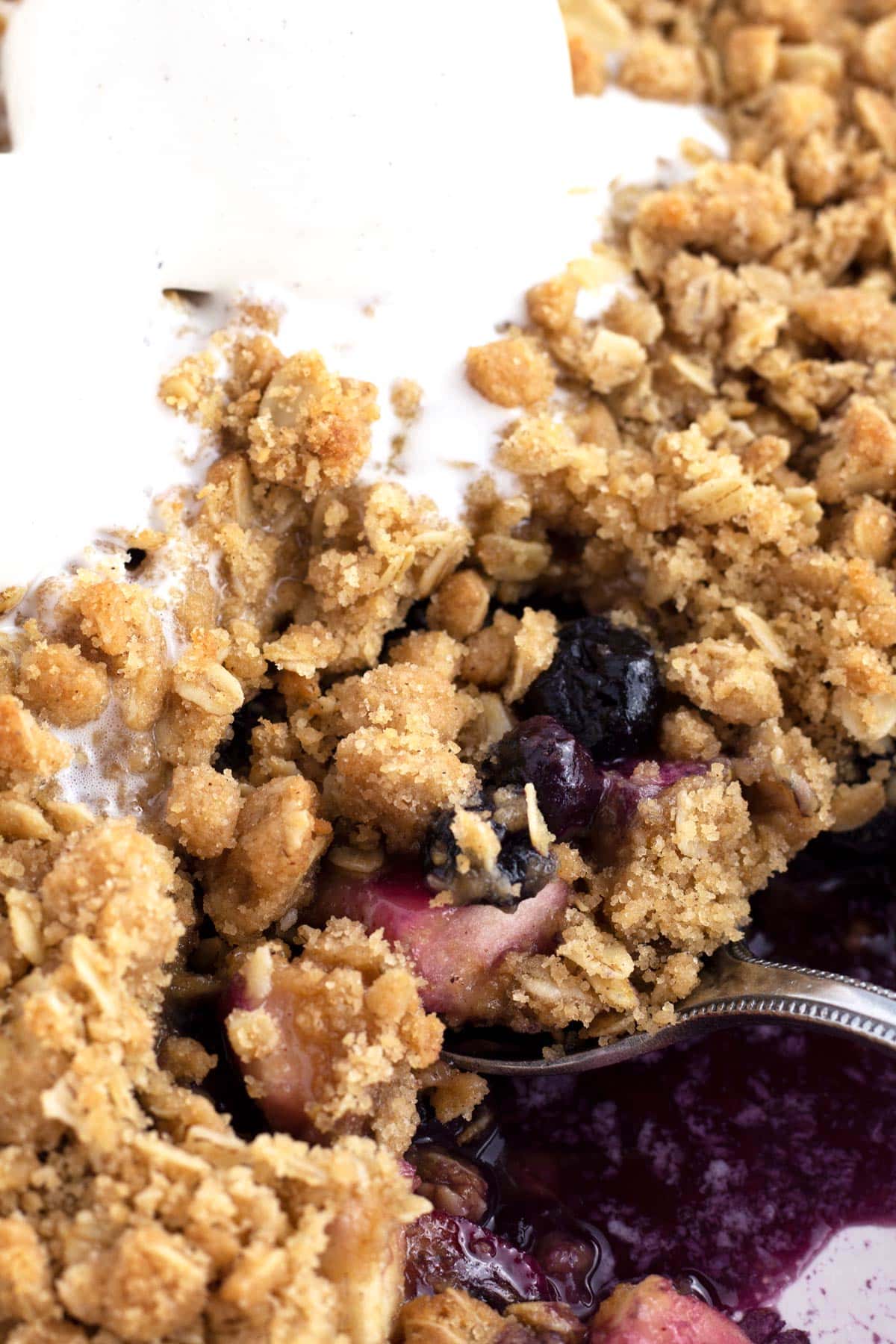 Close up of spoon scooping apple and blueberry crumble from a baking dish.