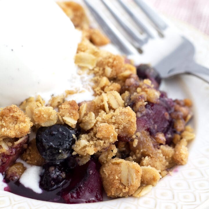 White plate piled with apple and blueberry crumble and a scoop of vanilla ice cream.