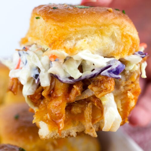 Chicken slider topped with coleslaw in a hand.