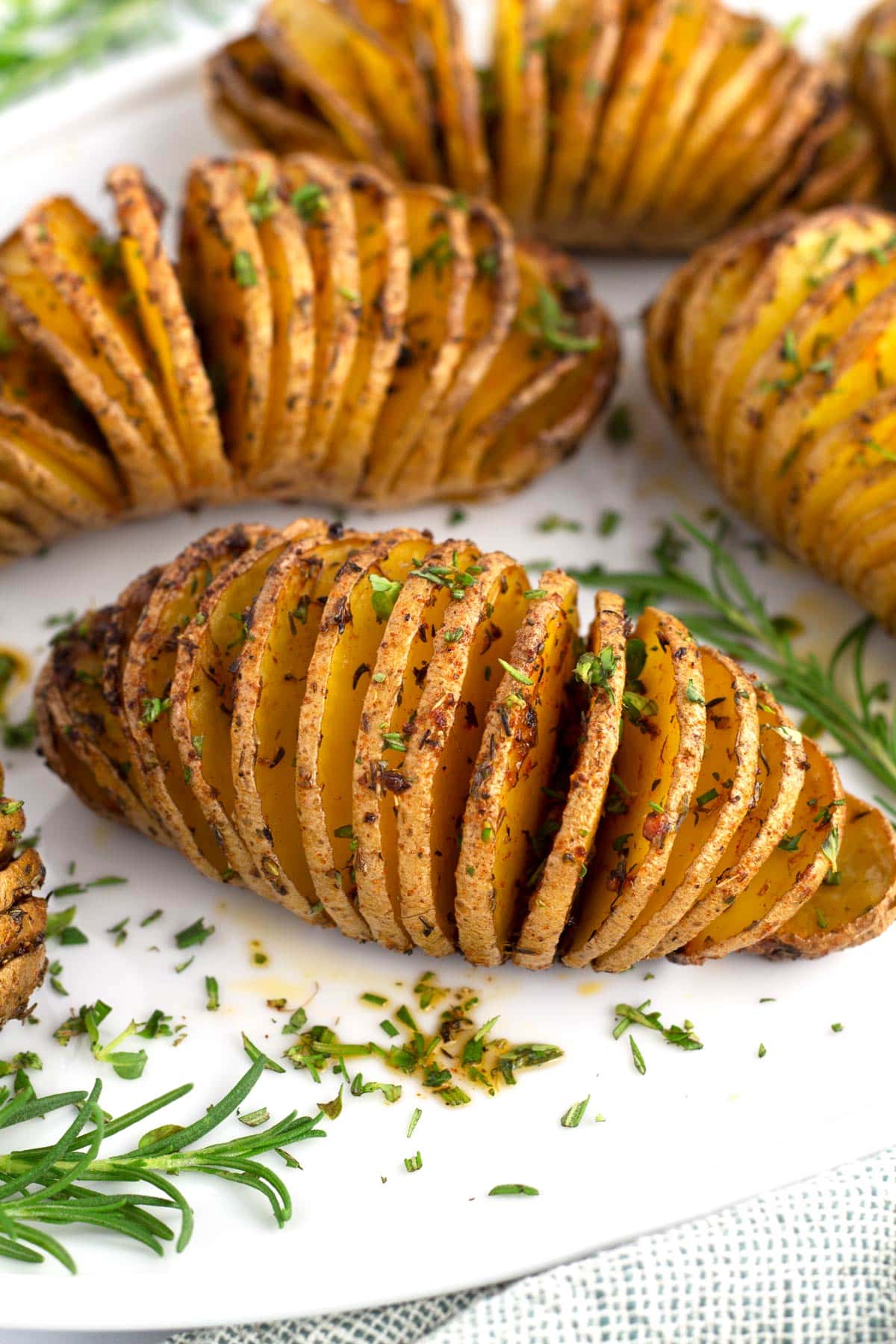 Crispy hasselback potatoes on white platter with fresh herbs sprinkled on top.