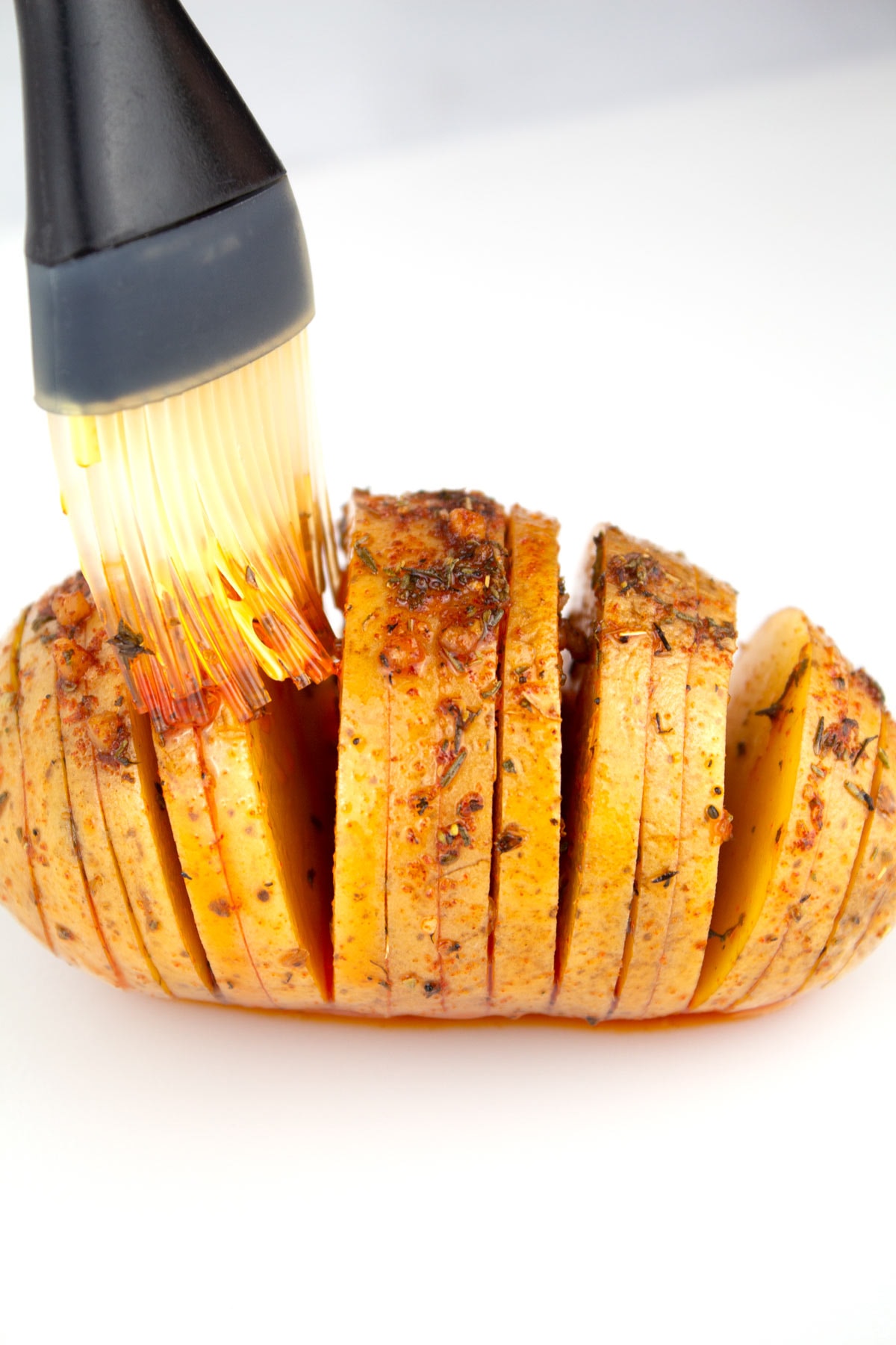 Silicone brush coating a potato with oil and seasonings.
