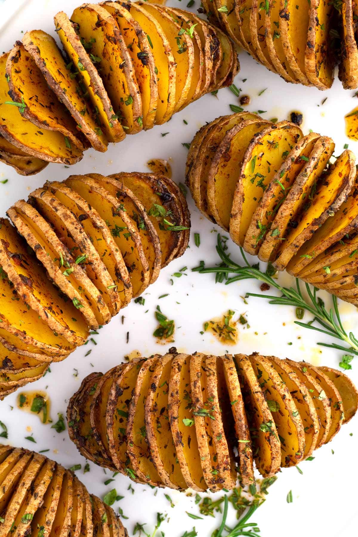 Overhead of six golden brown hasselback potatoes sprinkled with fresh herbs.