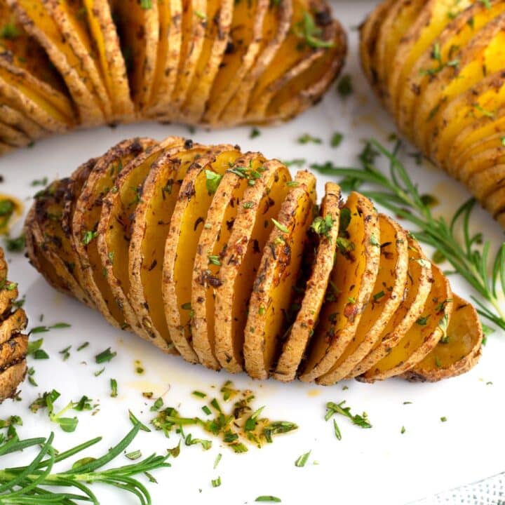 Hasselback potatoes on white platter with fresh herbs sprinkled on top.