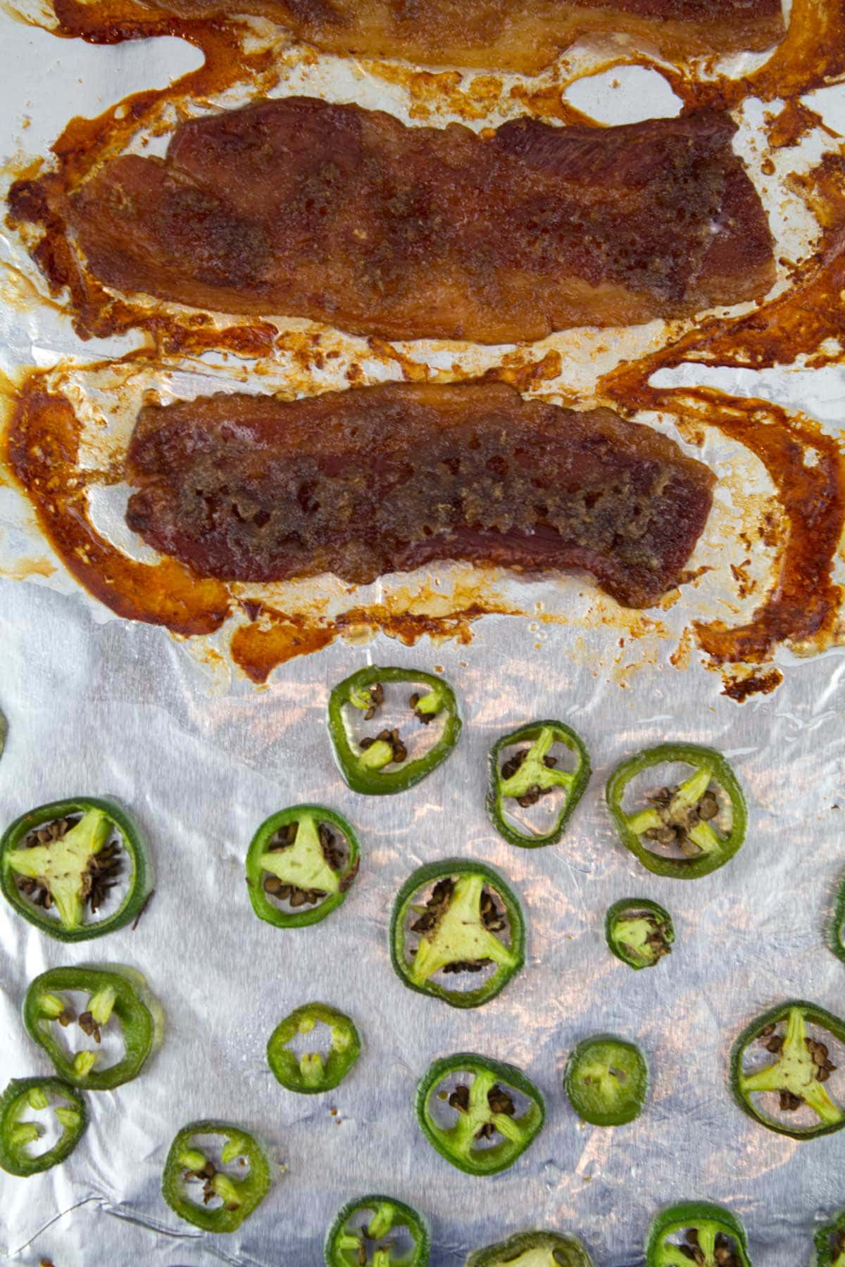 Baking sheet with roasted jalapeno slices and pieces of candied bacon just out of the oven.
