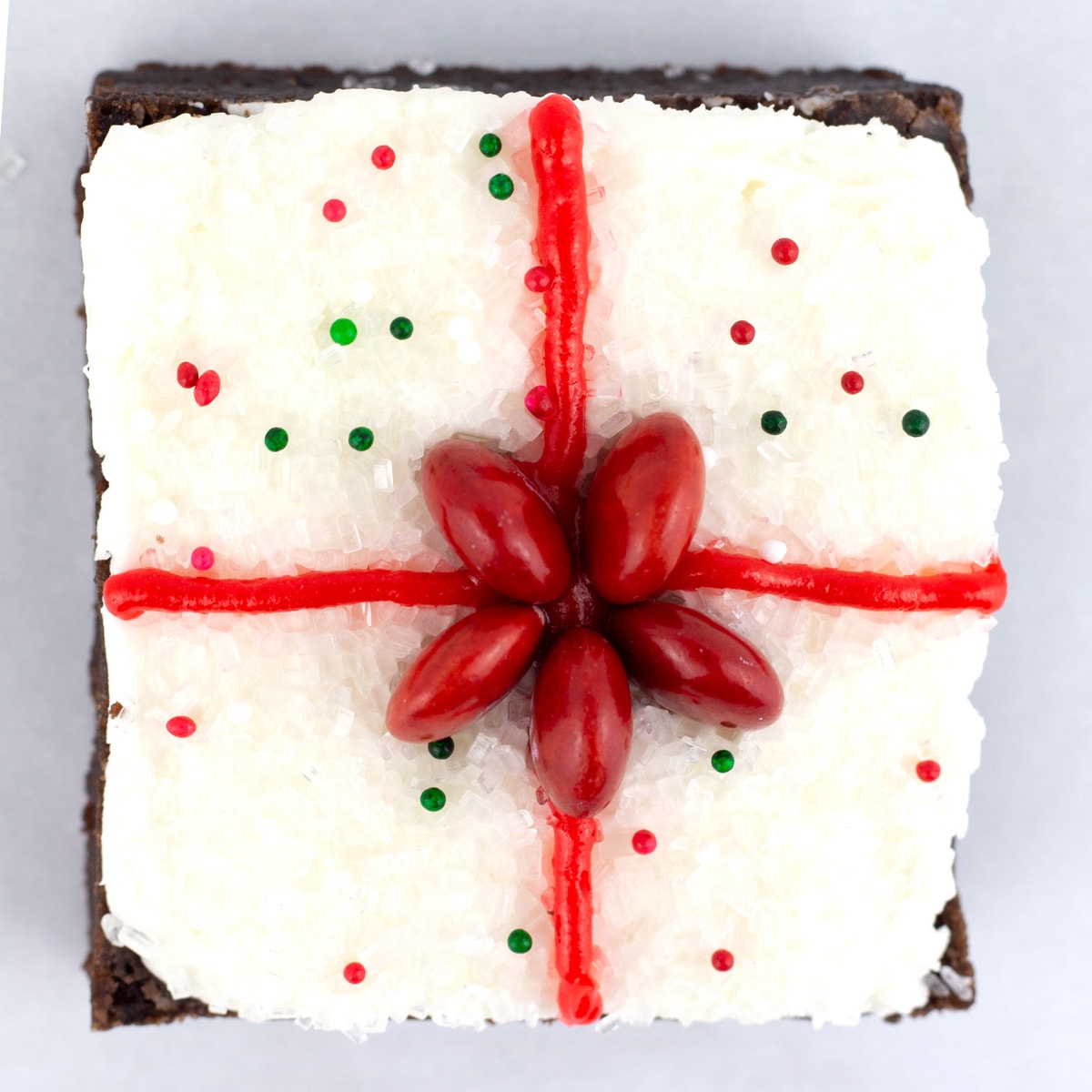A square brownie decorated as a Christmas present with a red bow and circle sprinkles.