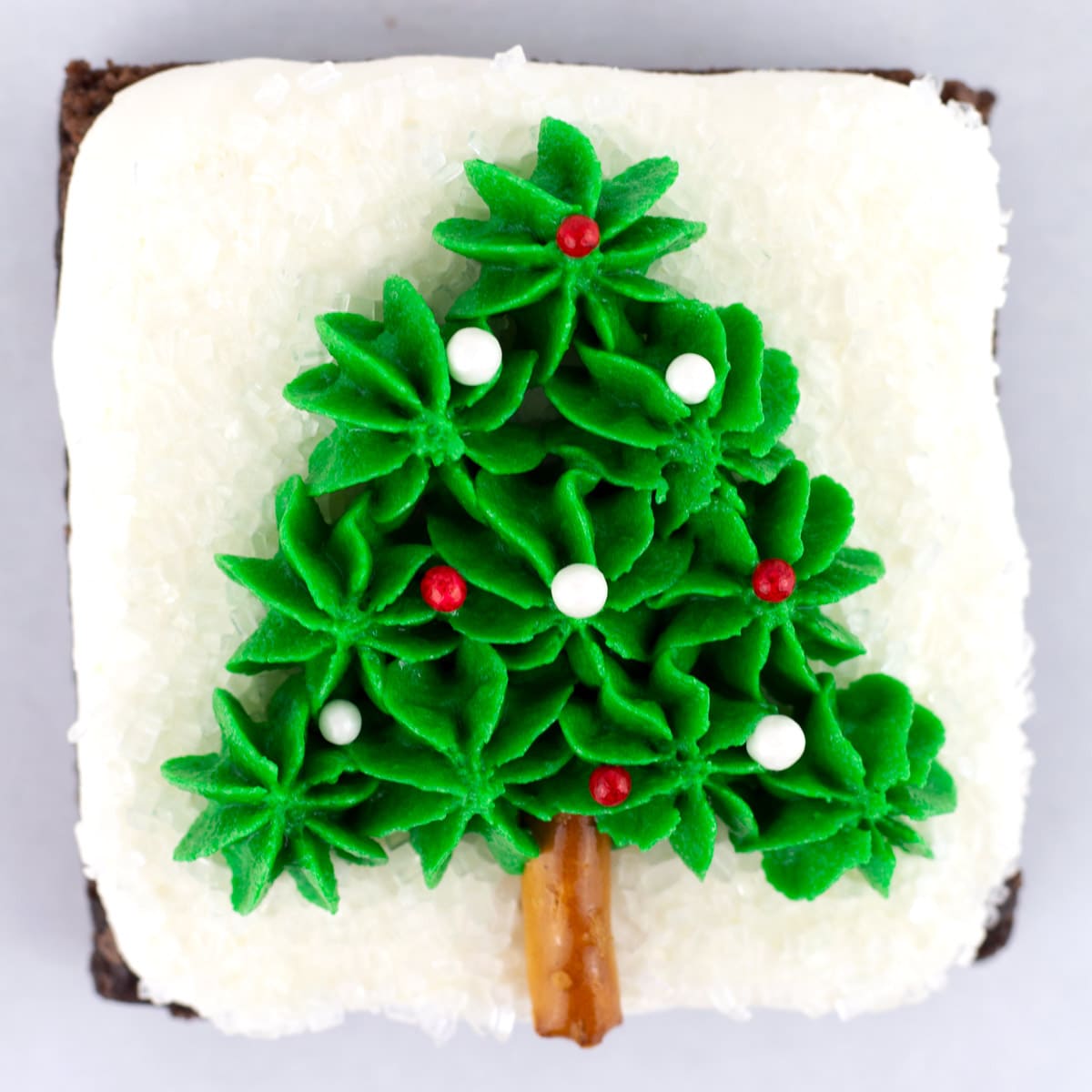 A square brownie decorated with a green Christmas tree and red and white sprinkles.