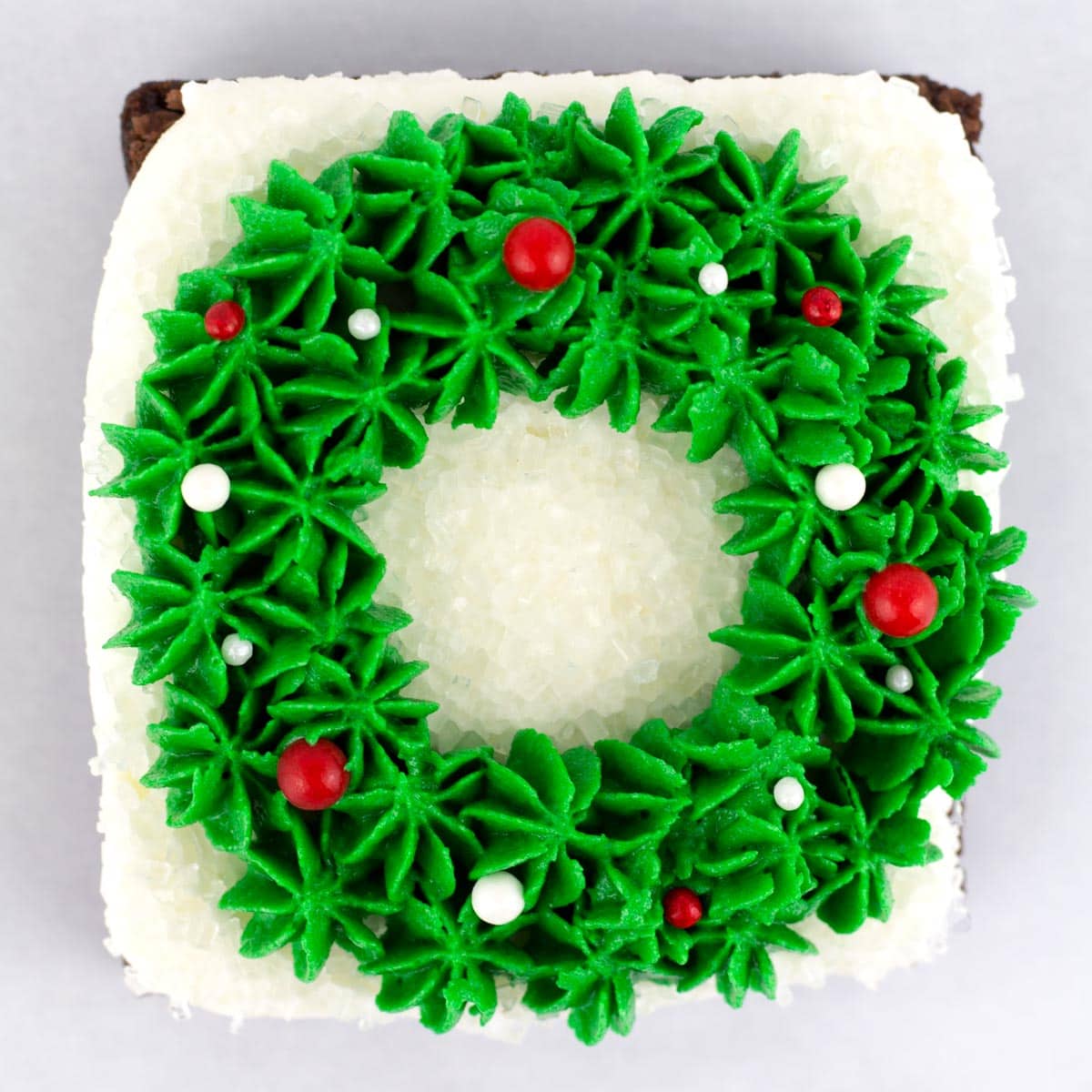 A square brownie with a Christmas wreath piped on top and decorated with red and white sprinkles.