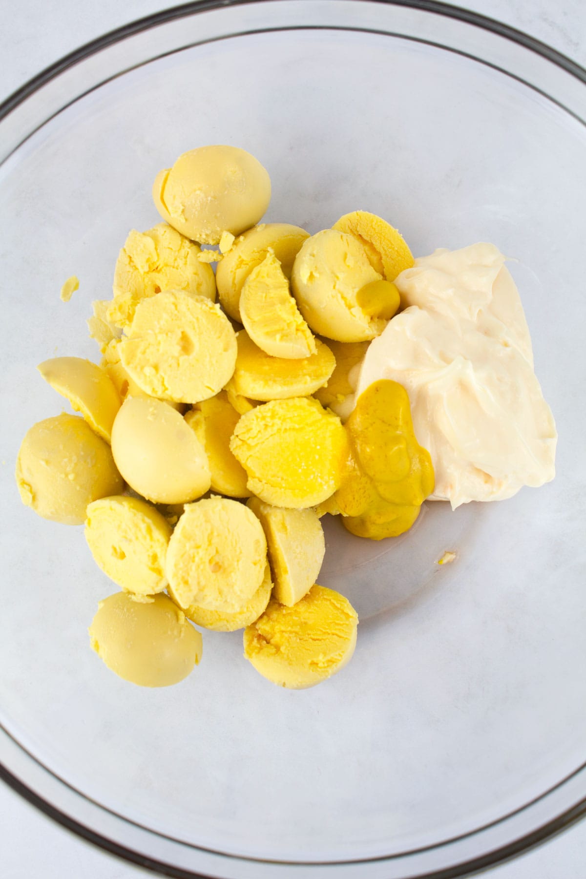 Yolks removed from hard boiled eggs and placed in a bowl with mayonnaise, mustard, and vinegar.